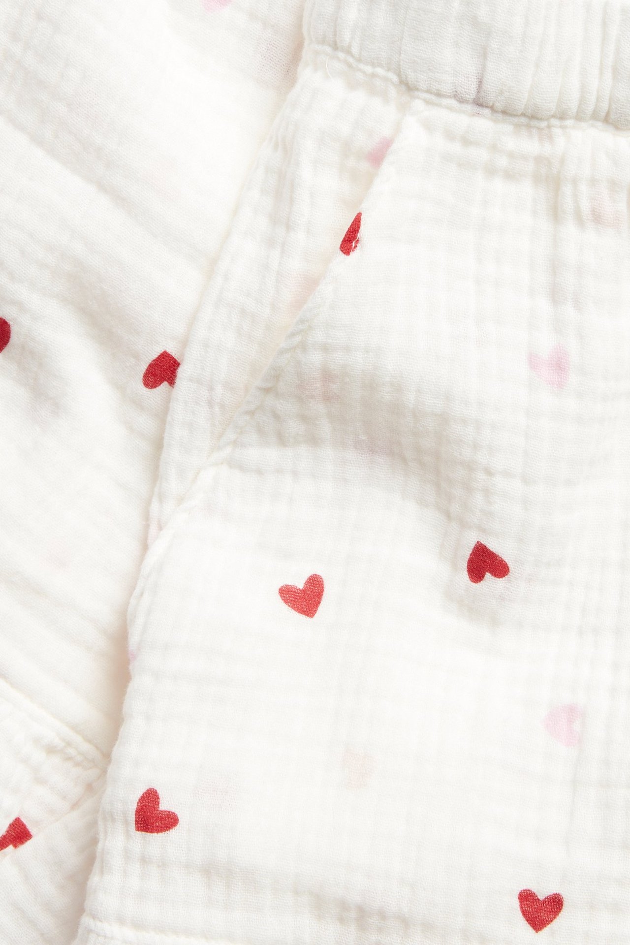 Lähikuva valkoisista puuvillapyjamashortseista punaisilla sydämillä, joustovyötäröllä ja sivutaskulla.