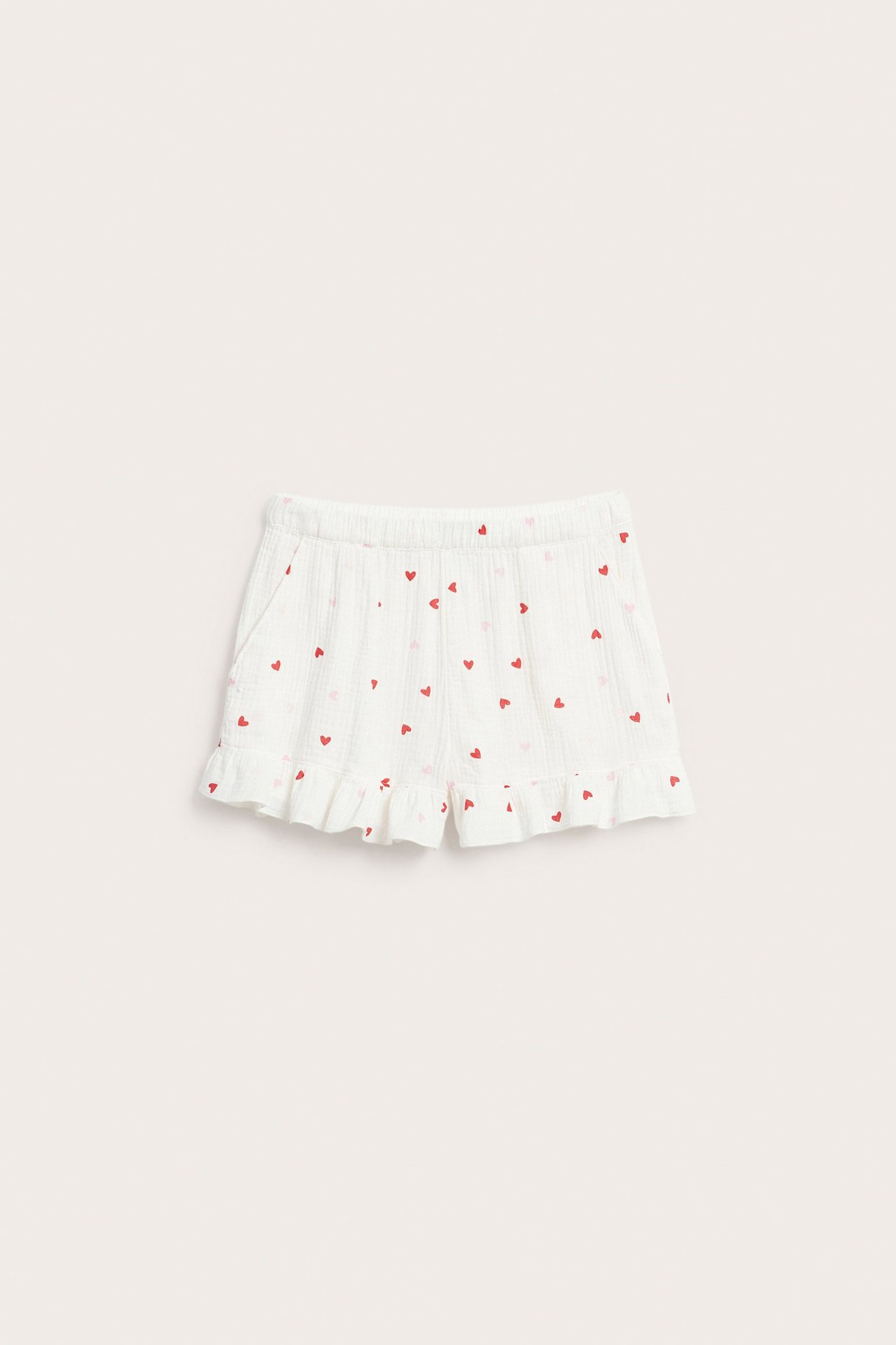 Edestä: Vaaleat puuvillaiset pyjamashortsit vaaleanpunaisella sydänkuviolla, joustovyötäröllä ja röyhelöreunalla.