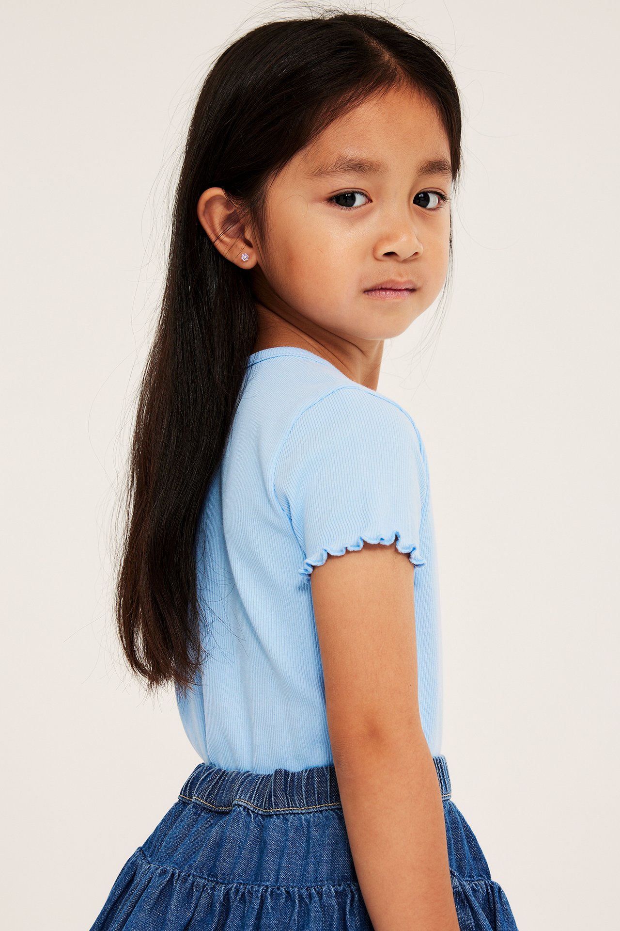 Sidebilde: Barn i lyseblå ribbet topp, mørkeblått denimskjørt og rosa øredobb.