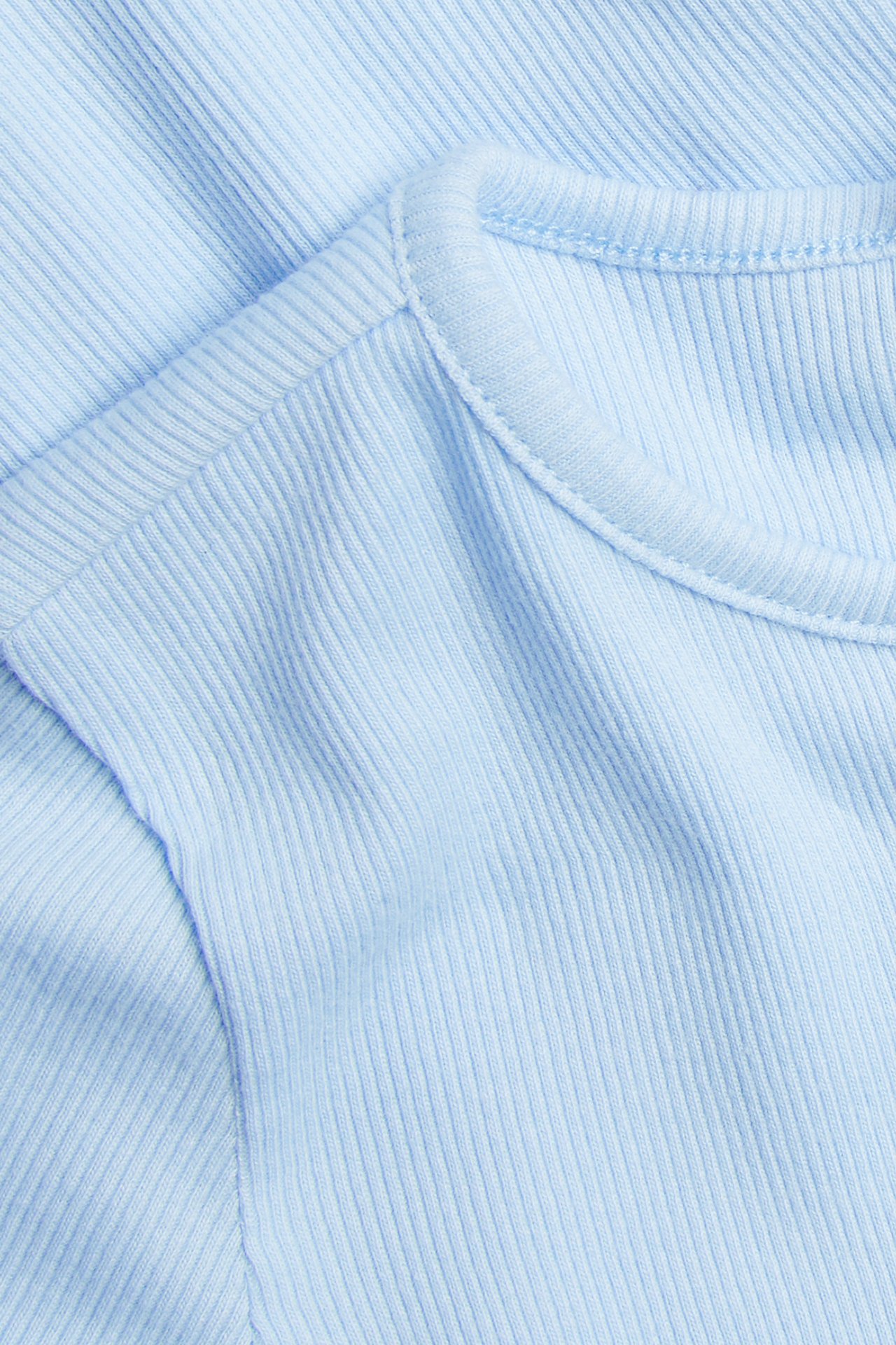 Nærbilde av en lyseblå ribbet kortermet topp i bomullstrikot med rund hals.
