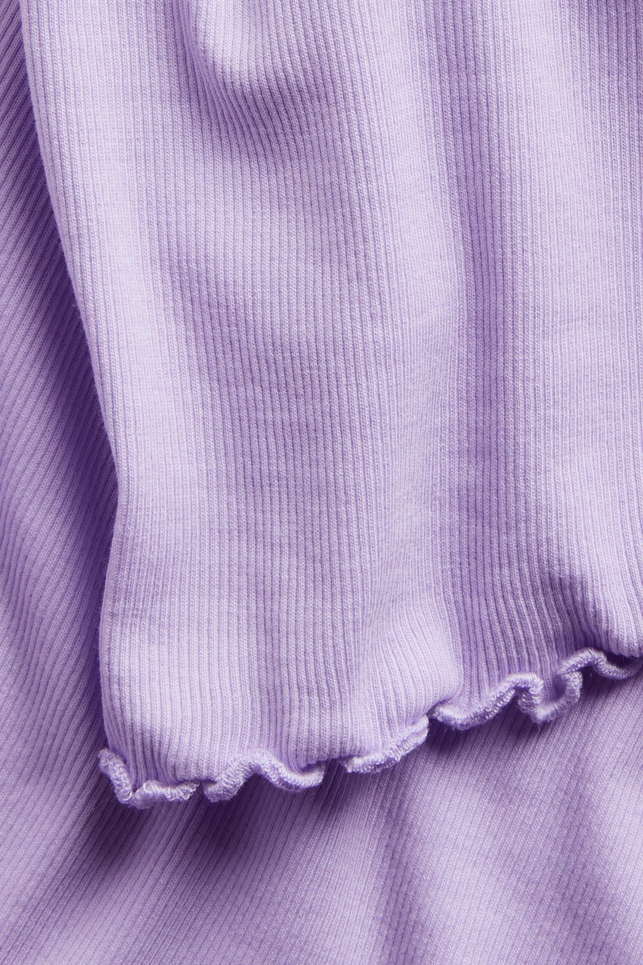 Zbliżenie jasnofioletowego, prążkowanego topu z krótkim rękawem z dzianiny bawełnianej z wykończeniem babylock na dole.