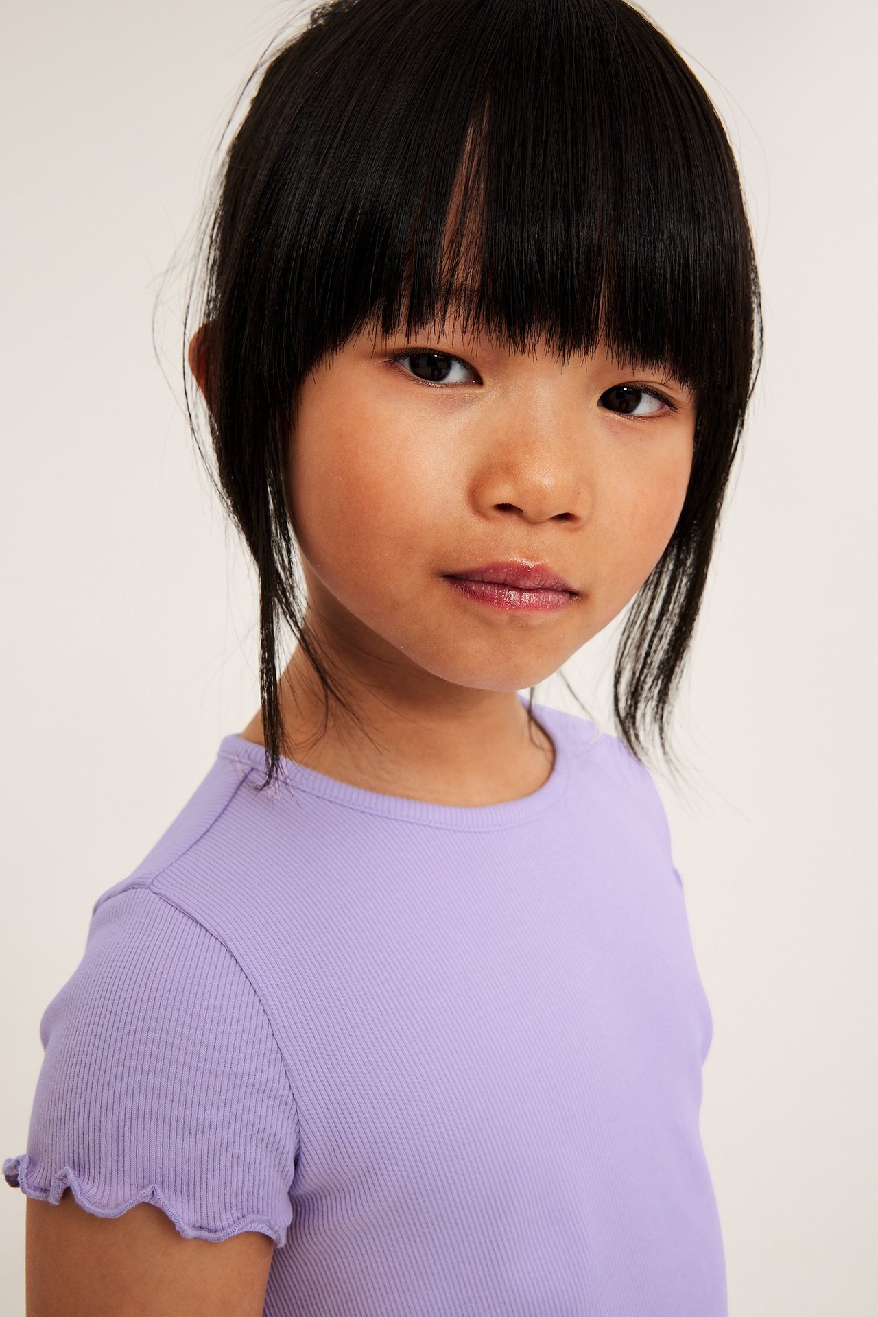 Z bliska, widok z przodu: dziecko nosi jasnofioletowy prążkowany top z babylockowymi brzegami.