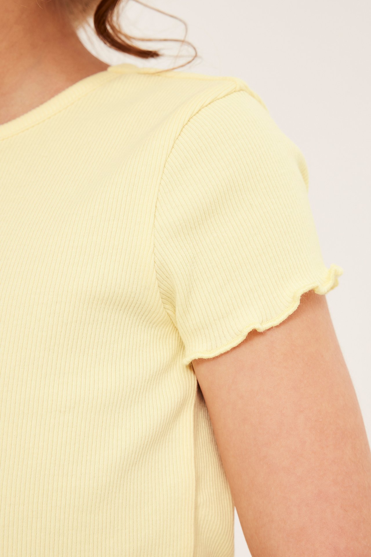 Lähikuva lapsesta yllään vaaleankeltainen ribattu lyhythihainen toppi, jossa babylock-reunukset hihansuissa.