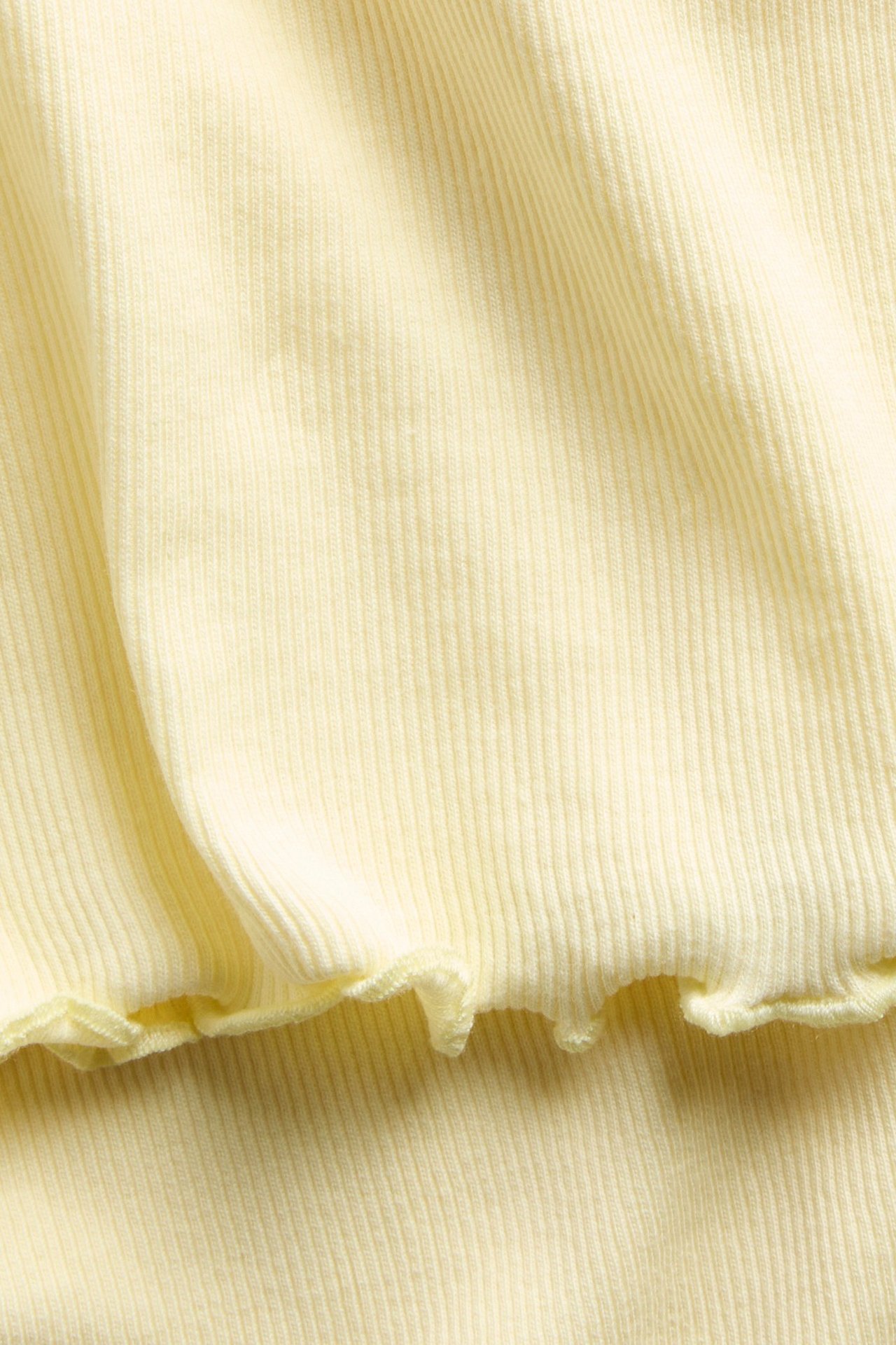 Lähikuva vaaleankeltaisesta ribbineulepuserosta, jossa on babylock-yksityiskohta helmassa.