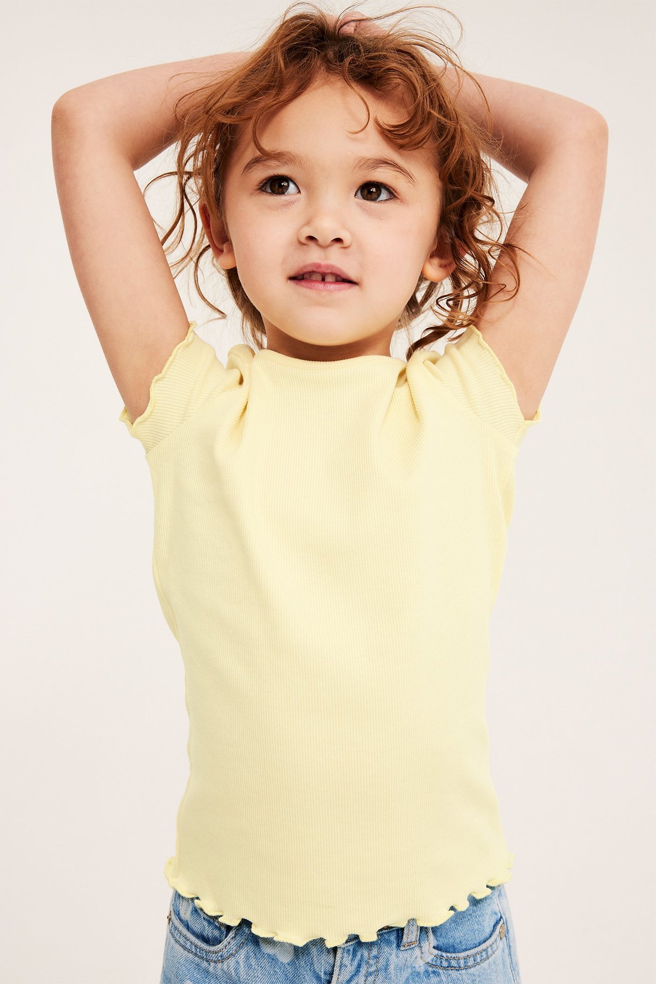Frontvy: barn bär en ljusgul ribbad kortärmad topp med babylockkanter och ljusblåa jeans.