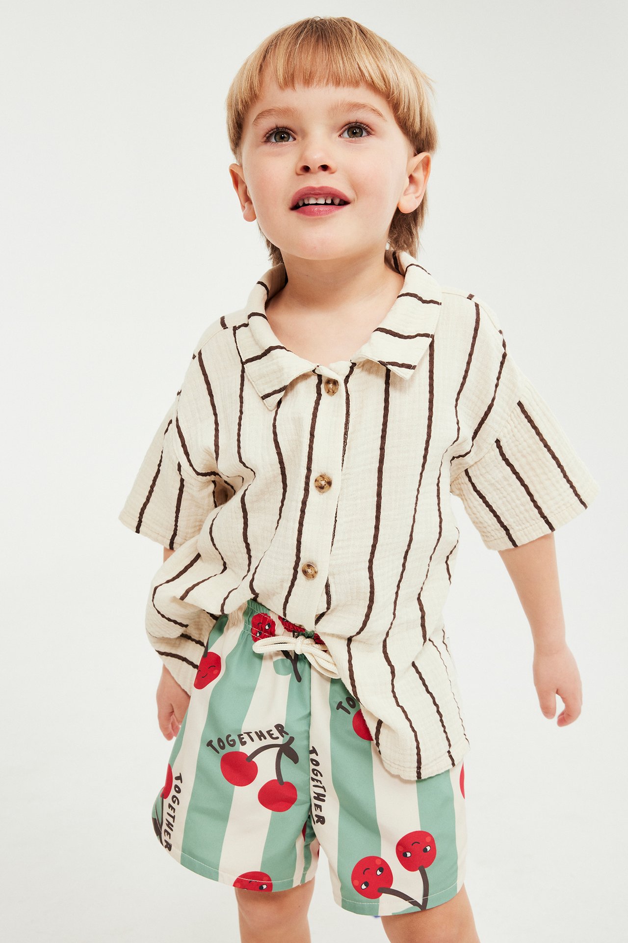 Framsida: Barn i mintgröna och vita randiga badshorts med körsbär, matchat med en off-white randig skjorta.