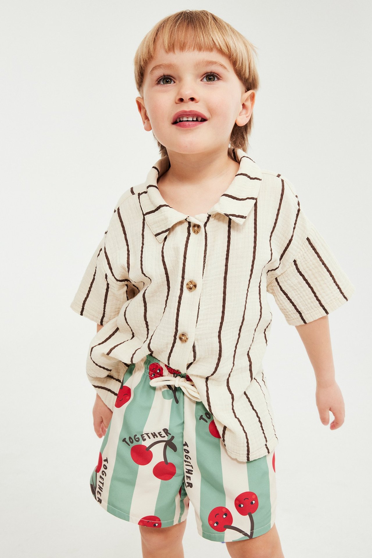 Framsida: Barn i mintgröna och vita randiga badshorts med körsbär, matchat med en off-white randig skjorta.