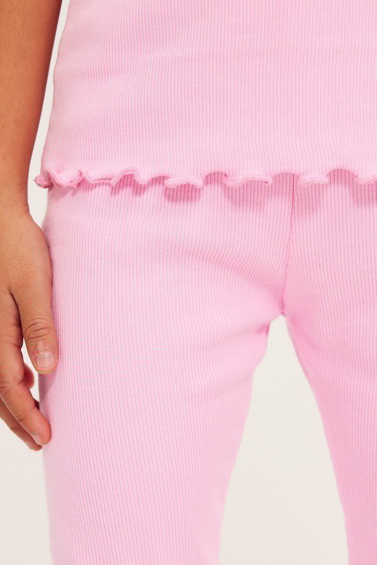 Närbild på barn i ljusrosa ribbade leggings och en matchande topp med vågig nederkant.