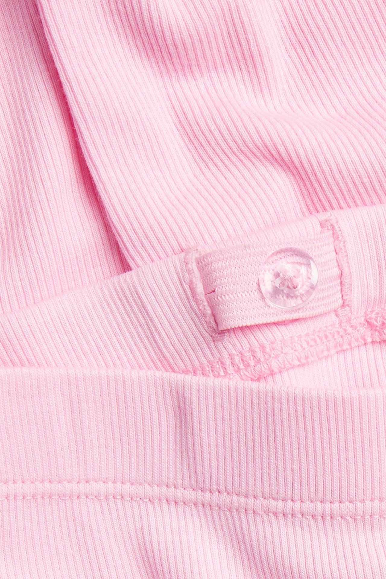 Zbliżenie na jasnoróżowe legginsy w prążki, ukazujące regulowaną talię z przezroczystym guzikiem.