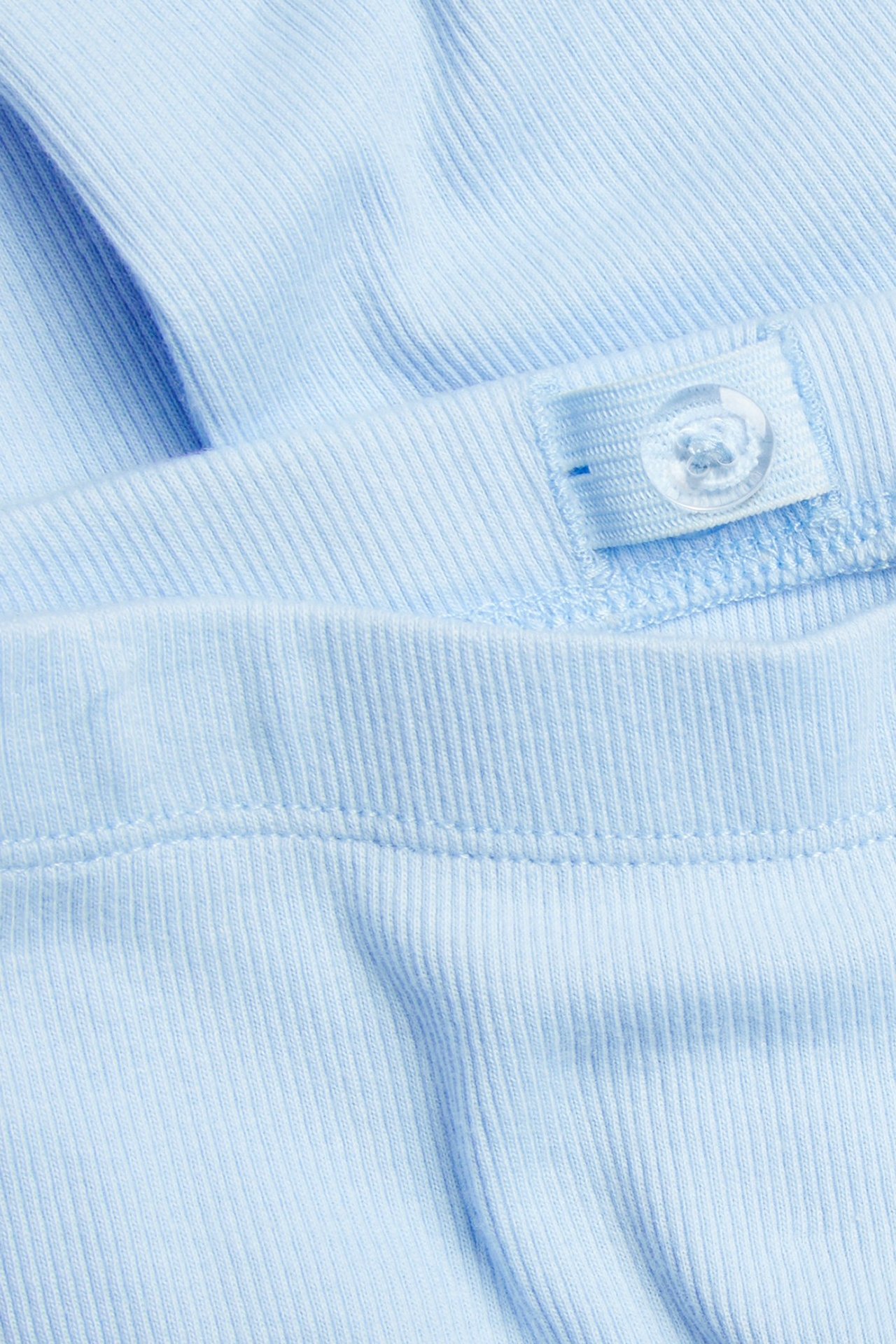 Zbliżenie na jasnoniebieskie prążkowane legginsy, pas z regulowaną gumką i guzikiem.