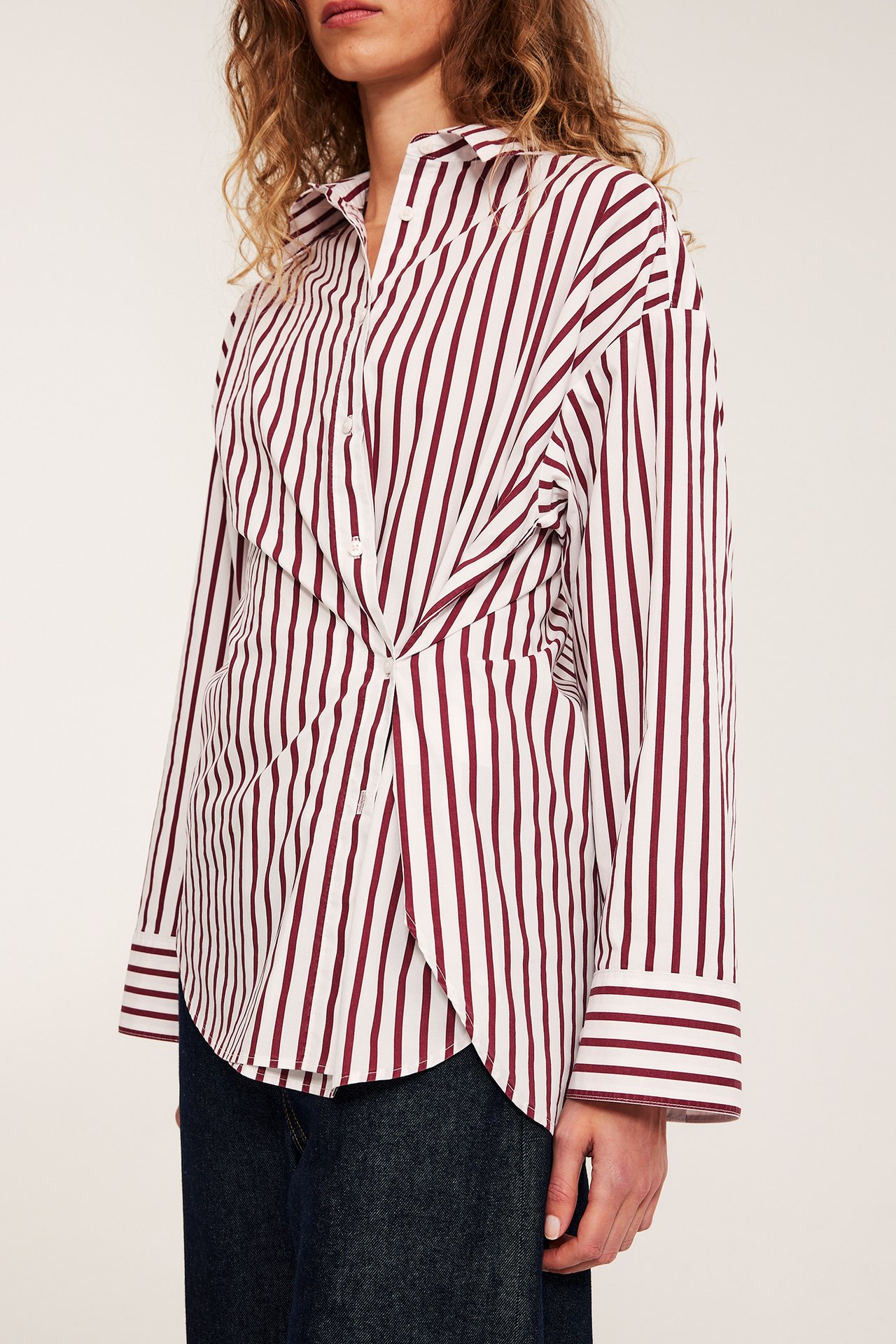 Nainen pukeutuu luonnonvalkoiseen, punaraitaan popliinipaitaan kierretyllä etuosalla, yhdistettynä tummansinisiin farkkuihin.