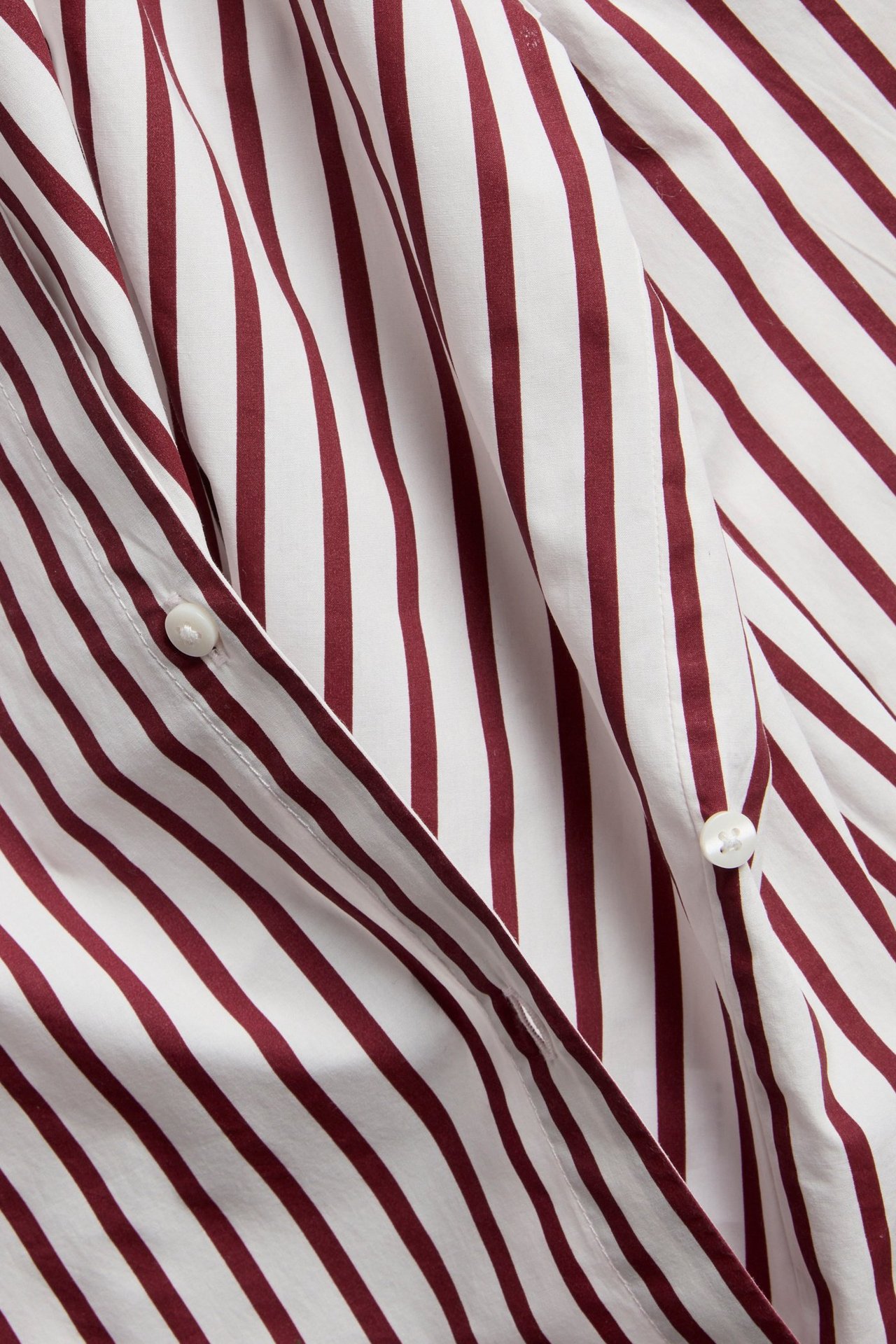 Zbliżenie na koszulę popelinową w paski ecru i ciemnoczerwone z guzikami i skośnym zapięciem.