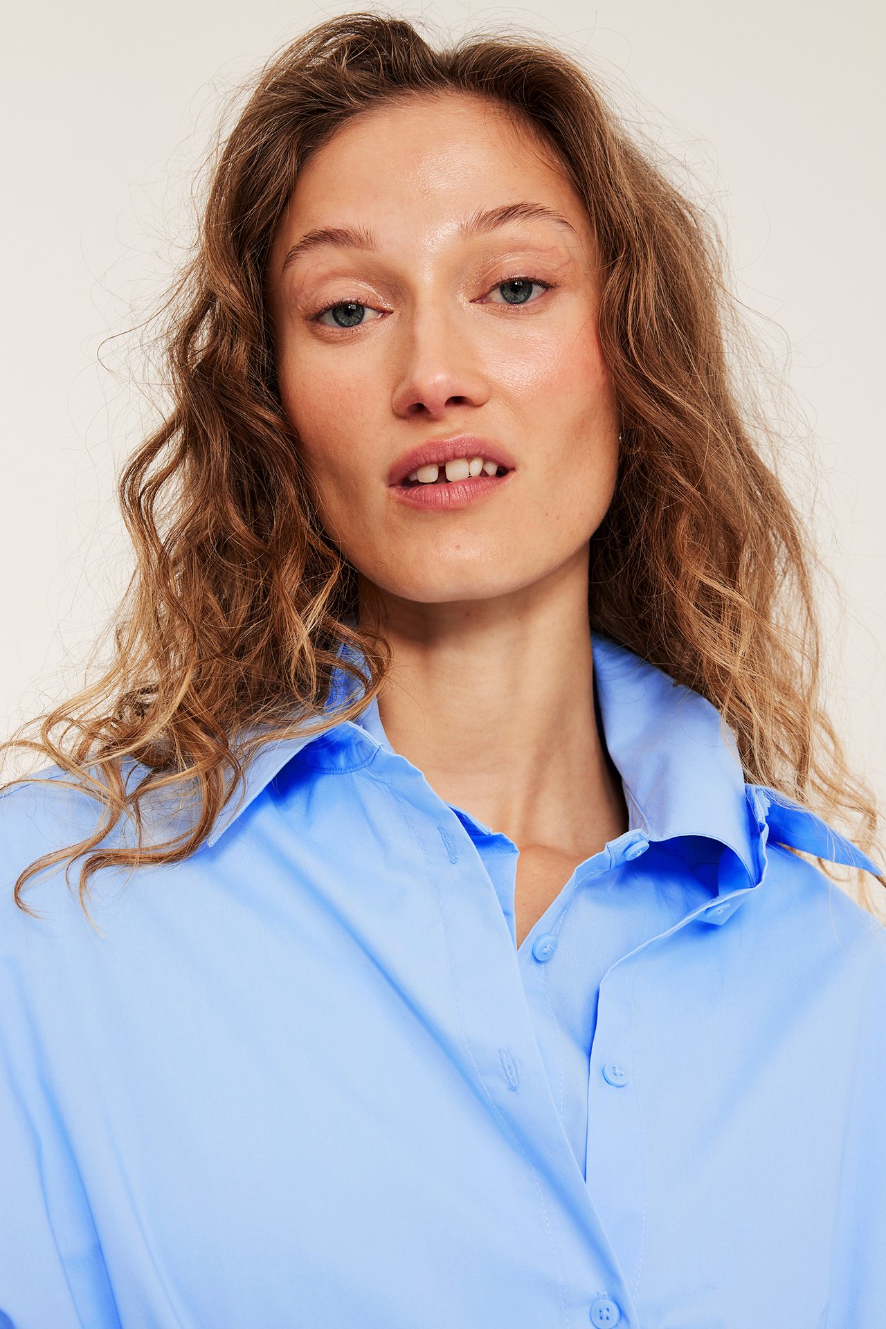 Lähikuva naisesta yllään vaaleansininen puuvillapopliinipaita, jossa kaulus ja nappikiinnitys.