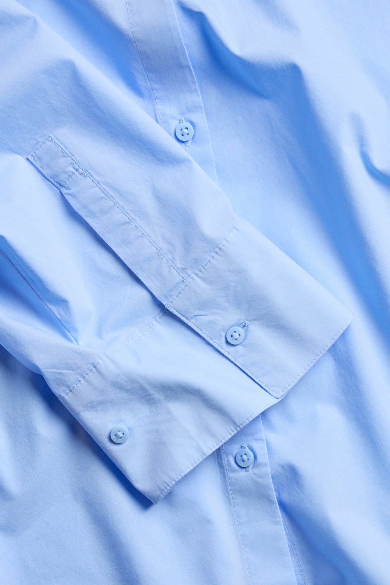 Zbliżenie na jasnoniebieską bawełnianą koszulę poplinową z widocznymi guzikami mankietu.