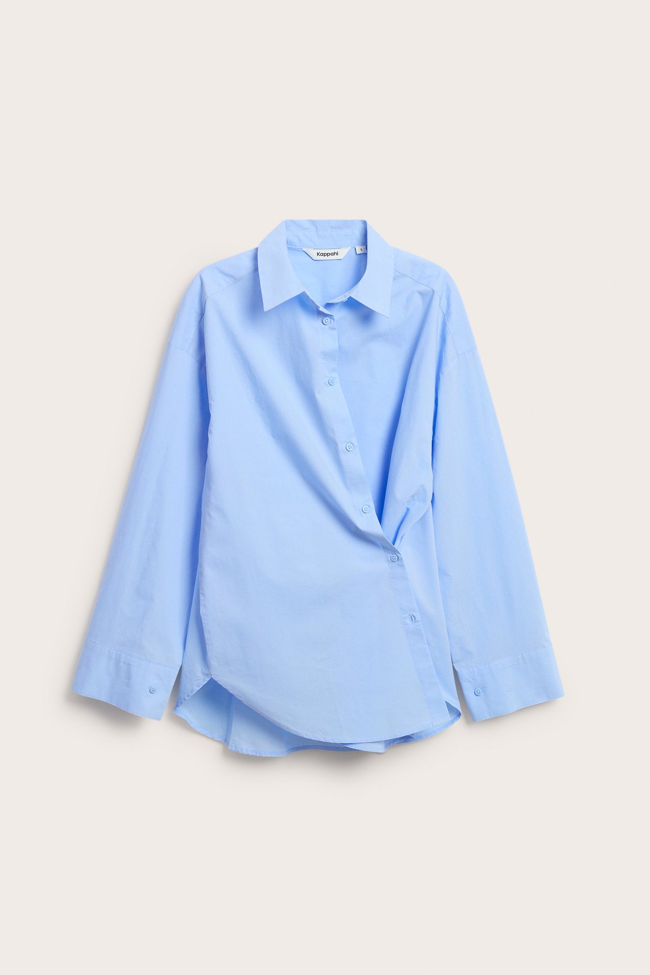 Edestä kuvattu vaaleansininen puuvillapopliinipaita, jossa epäsymmetrinen napitus.