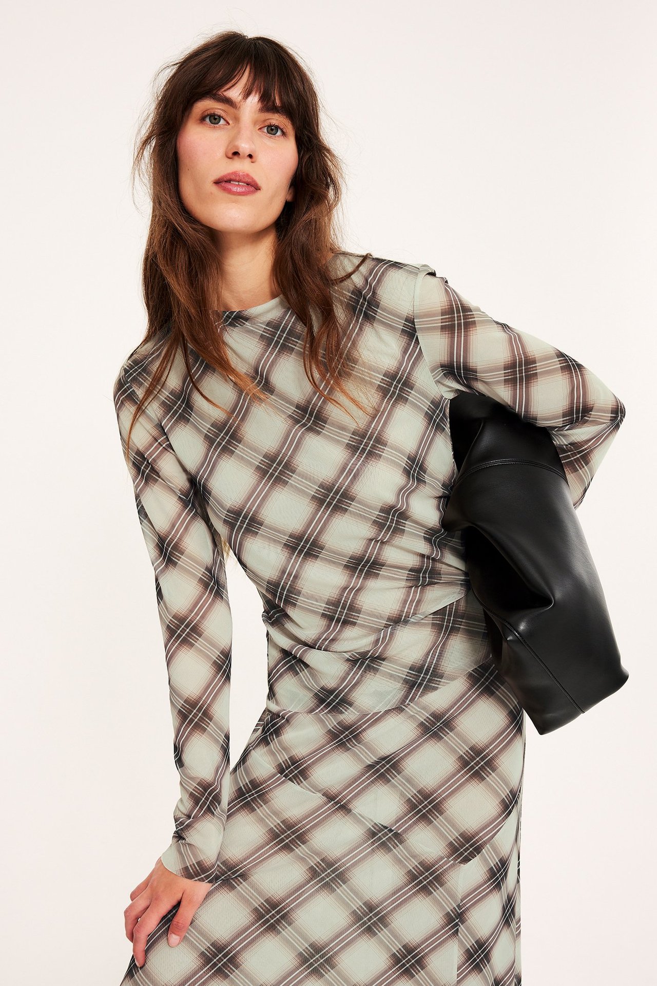 Nainen yllään beige ruudullinen verkkopitkähihainen toppi, yhteensopiva hame ja pitää mustaa käsilaukkua.