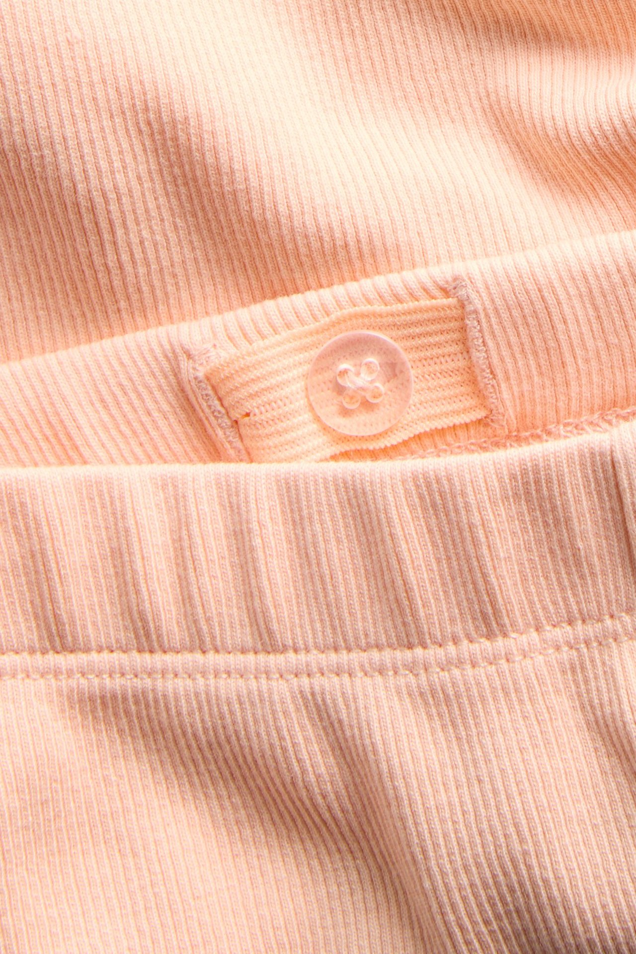 Lähikuva vaaleanoransseista ribbatuista pyöräilyleggingseistä, joissa on säädettävä vyötärö nappi ja kuminauha.