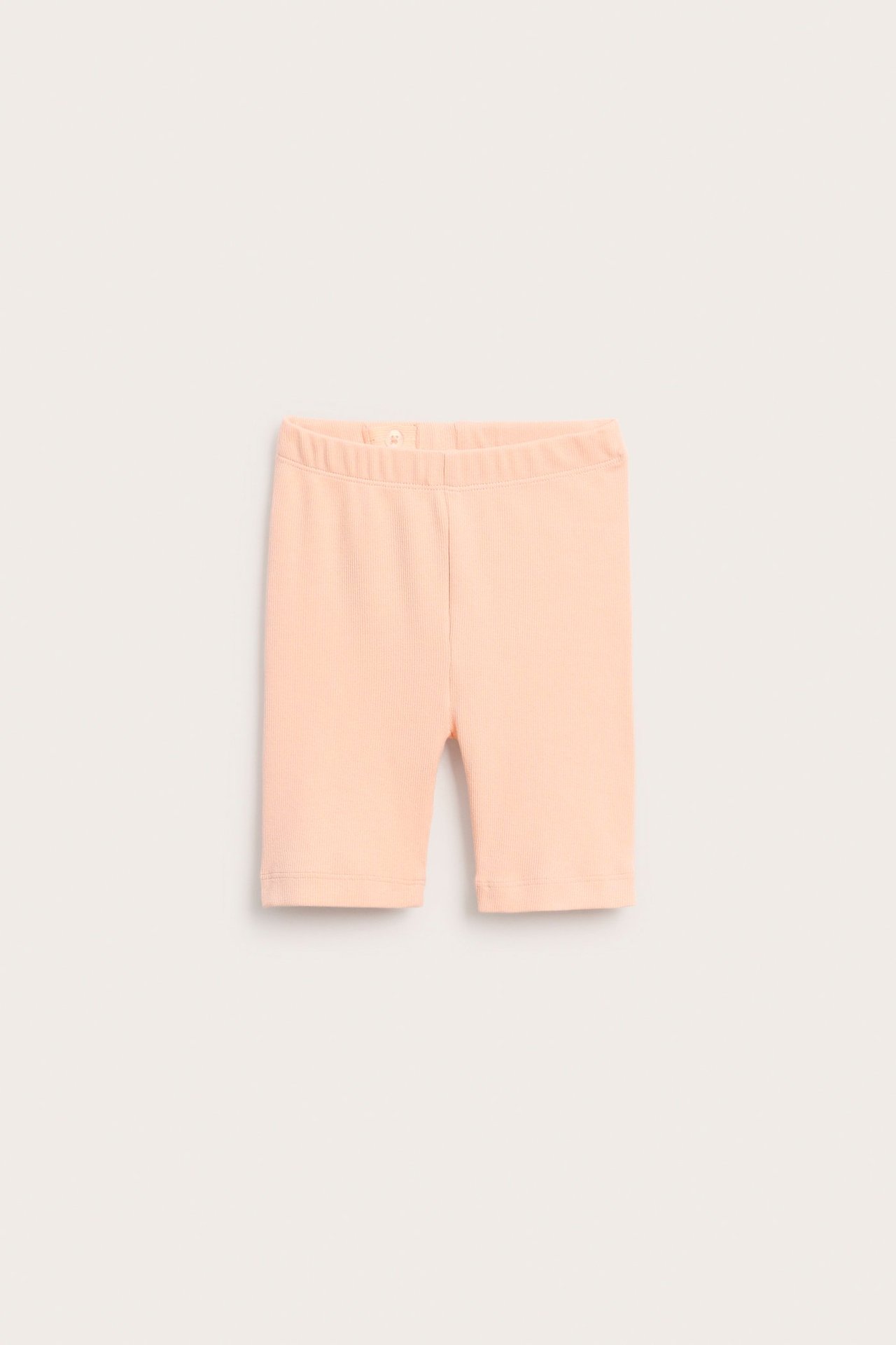 Edestä näkymä vaaleanoransseista ribbipuuvillaisista lasten pyöräilyshortseista joustovyötäröllä.