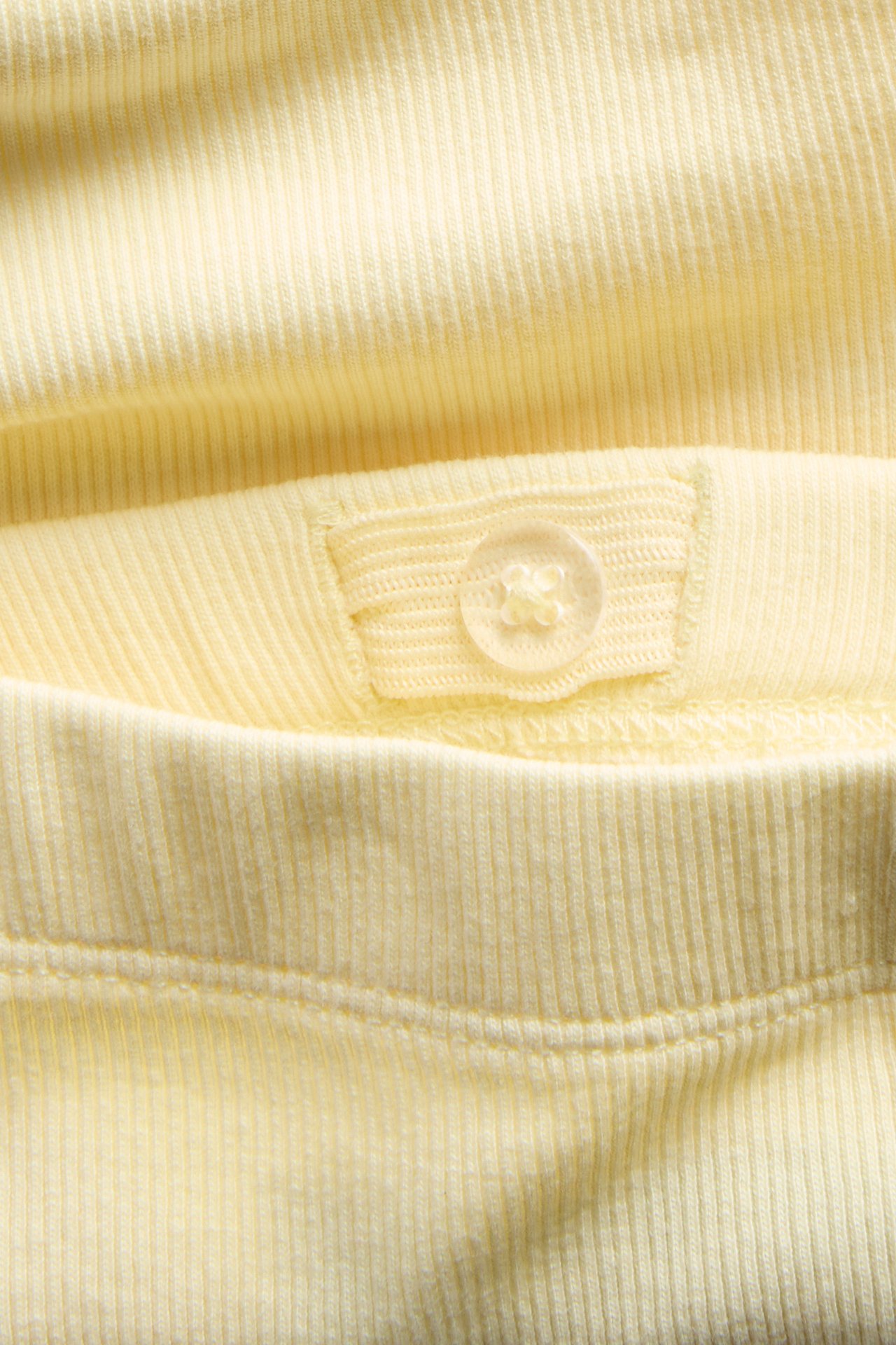 Närbild av ljusgula ribbade cykelbyxor med justerbar resårmidja med knapp.