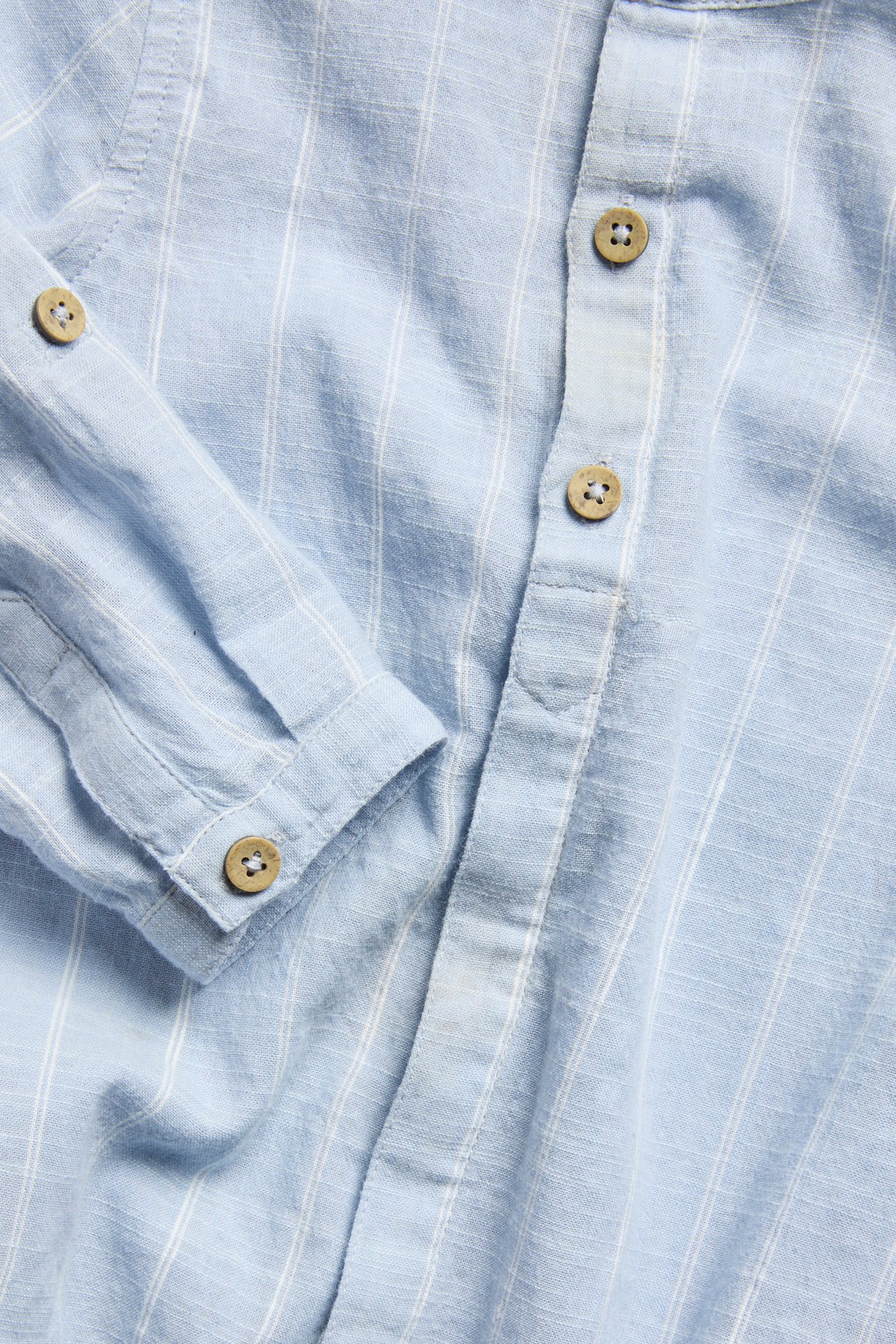 Närbild av en ljusblå randig långärmad skjortbody i bomull med träknappar framtill.
