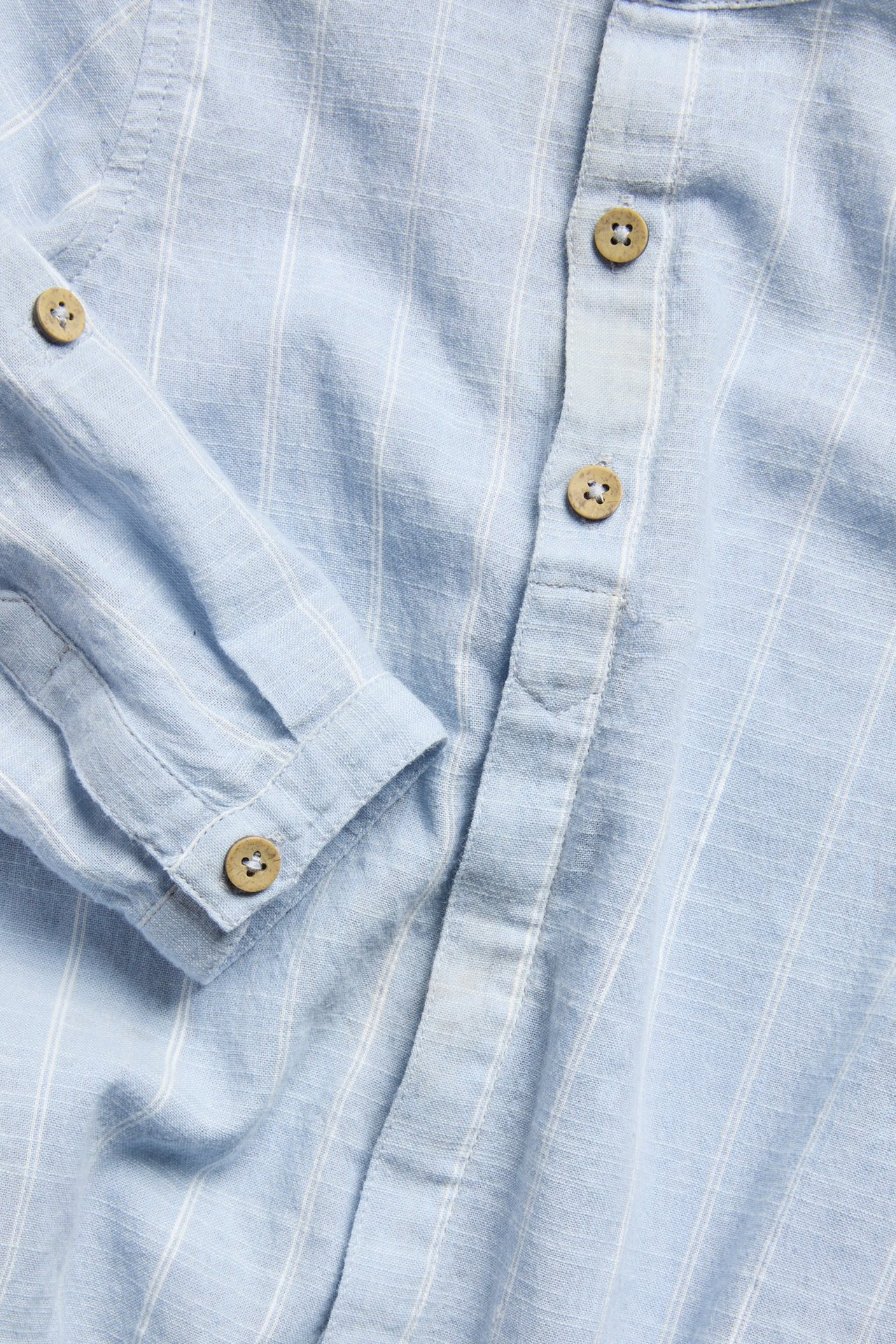 Zbliżenie jasnoniebieskiego bawełnianego body w paski z długim rękawem i drewnianymi guzikami.