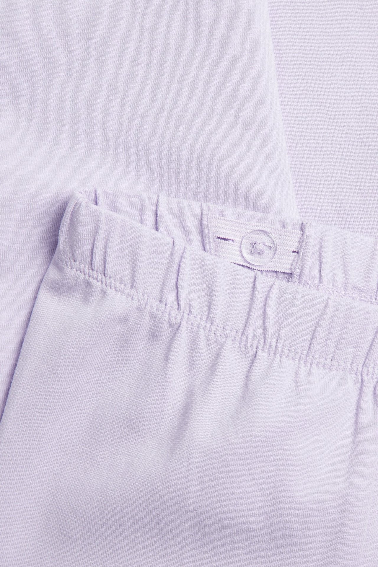 Närbild av ljusrosa caprileggings i bomullsmix, visar resår i midjan med justerbar knappdetalj.