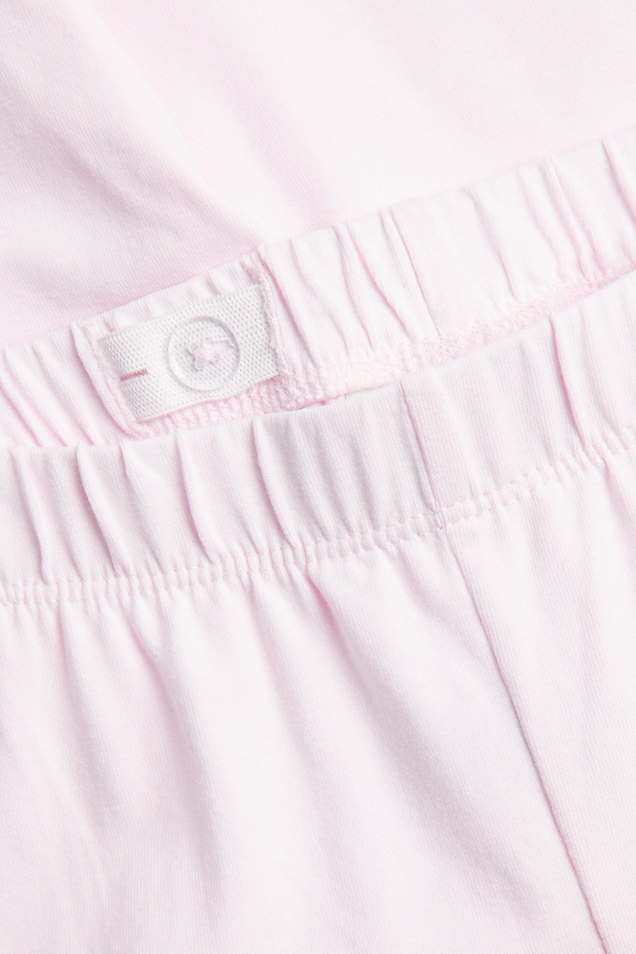 Närbild av ljusrosa caprileggings, resårlinning med vit knapp och justerbar flik.