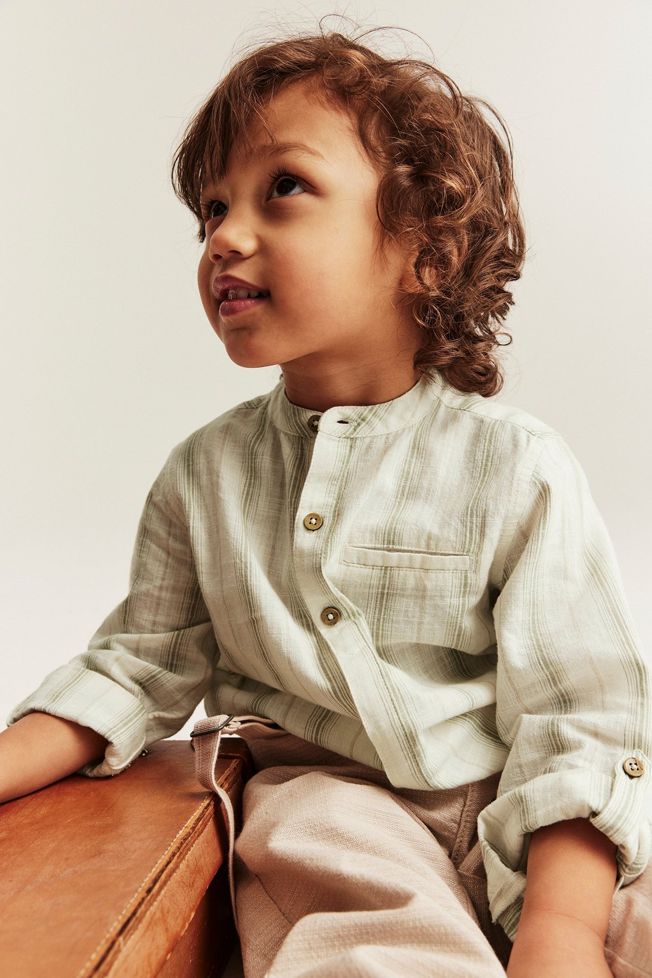 Närbild av barn i ljusgrön randig bomullsskjorta med murarkrage, upprullade ärmar och beige byxor.