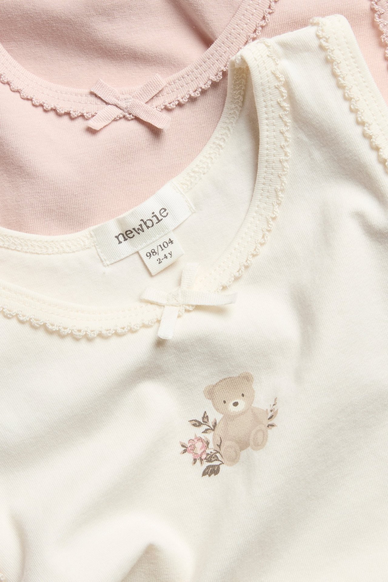 Enfärgad vit linne med rosett, rosett och liten björntryck, lång ärm, över vit t-shirt.
