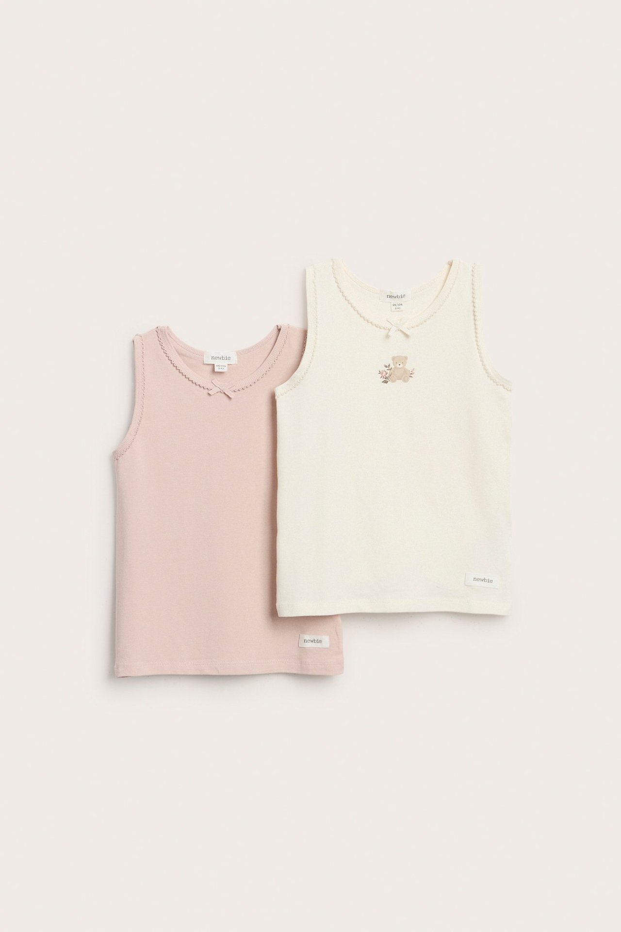 To ensfargede barne-topper, hvit og rosa, med rosetter og blondesøm.