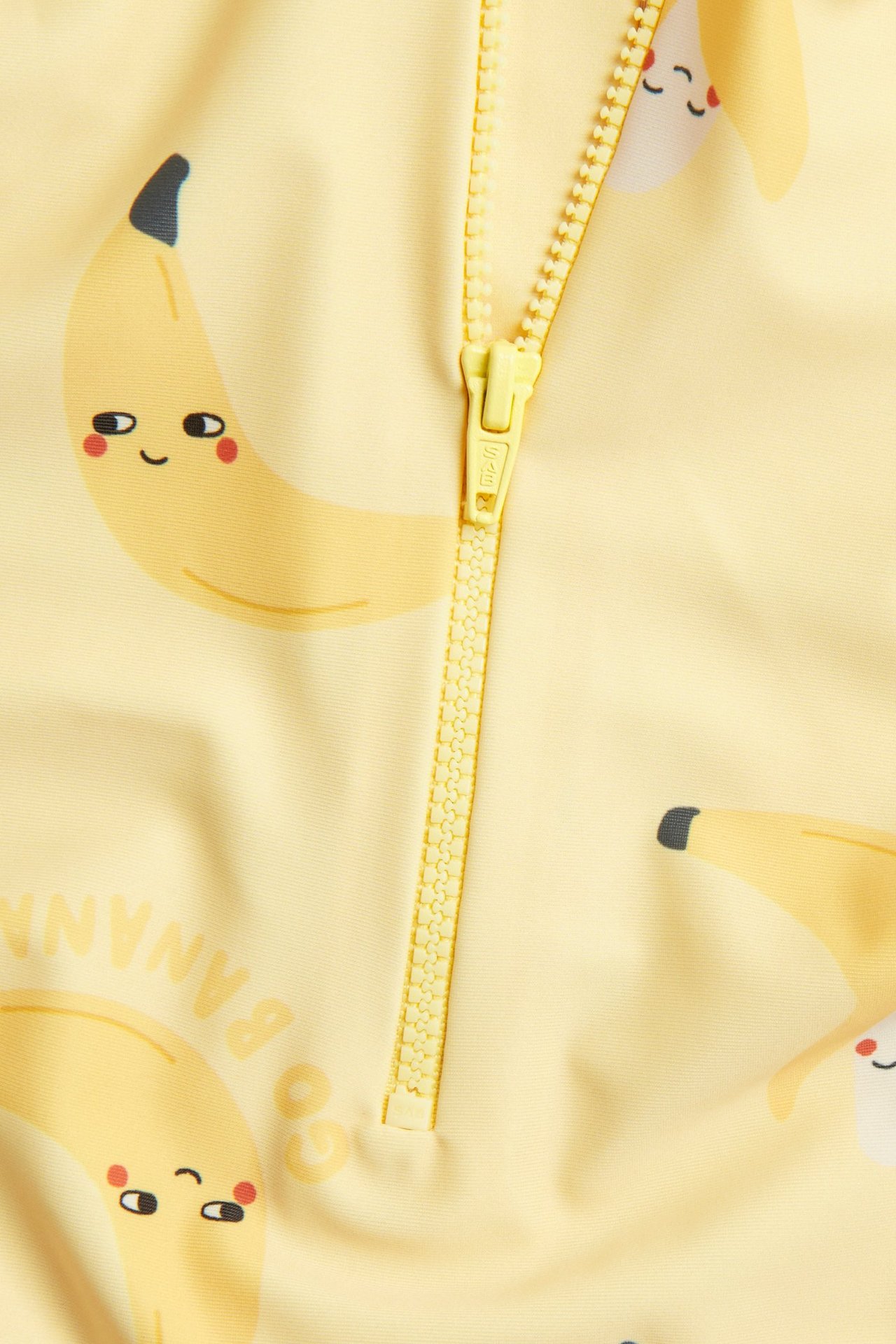 Lähikuva edestä keltaisesta vauvan UV-puvusta, jossa on banaanikuvio ja keltainen vetoketju.