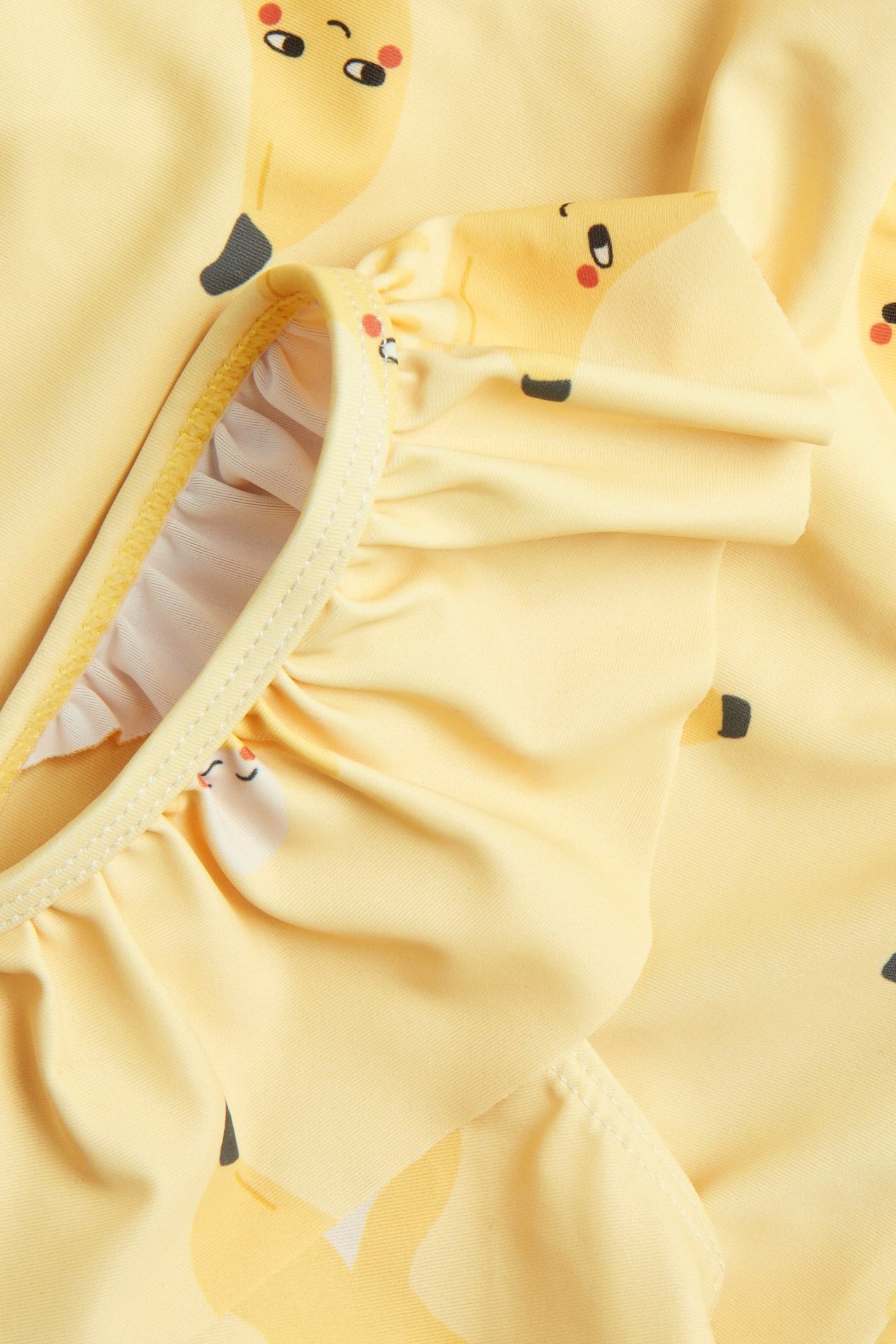 Lähikuva keltaisesta lasten uimapuvusta, jossa on röyhelöitä ja hauska banaanikuvio.