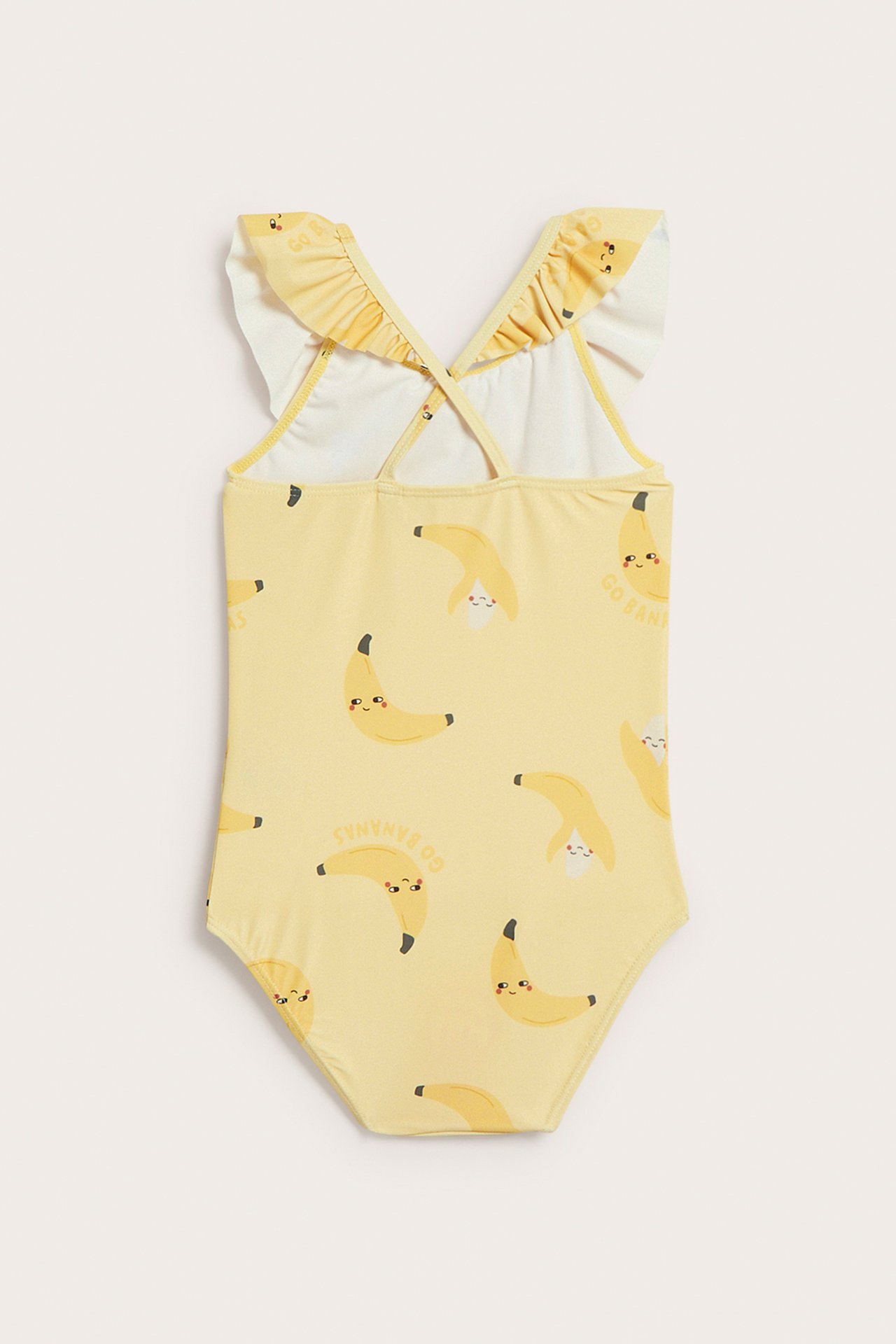 Takaapäin näkymä keltaisesta lasten uimapuvusta, banaanikuviolla, röyhelöillä olkaimissa ja ristiselkähihnoilla.