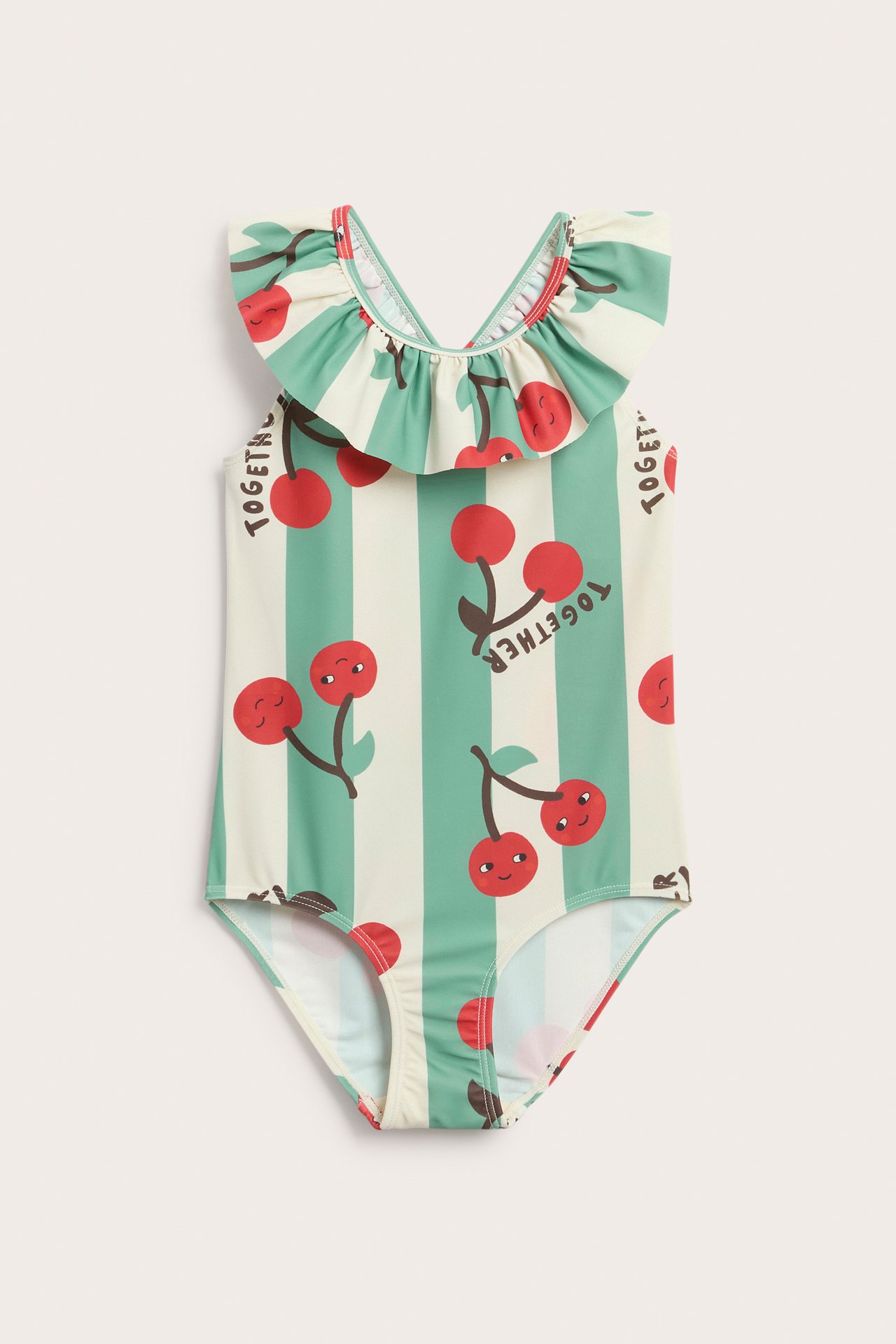 Framifrån, en barnbaddräkt i ljusbeige med gröna ränder, röda körsbär och volangkanter.