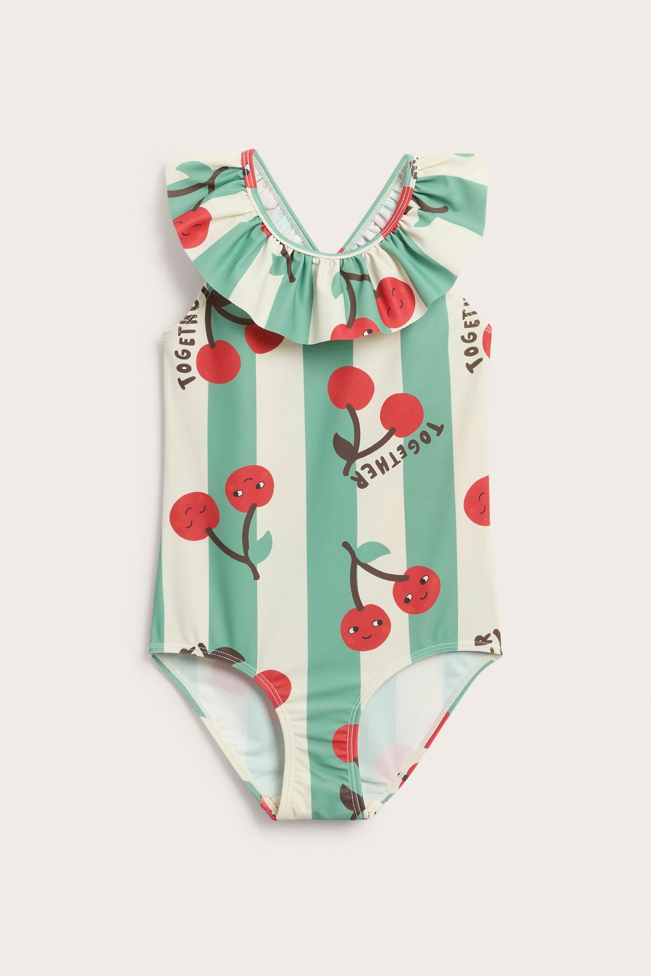 Framifrån, en barnbaddräkt i ljusbeige med gröna ränder, röda körsbär och volangkanter.