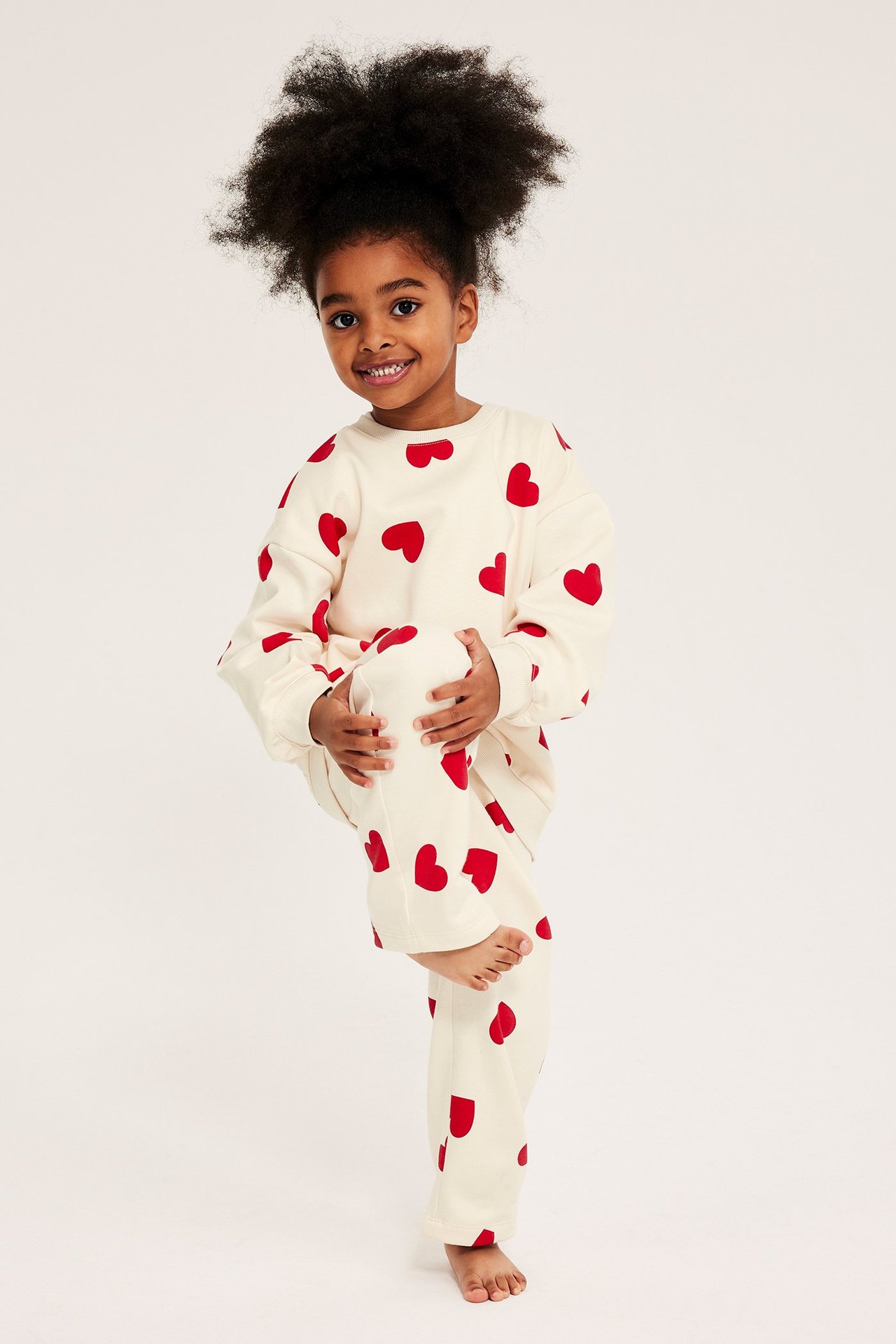Widok z przodu: dziecko w kremowej bluzie dresowej i pasujących spodniach w czerwone serca.