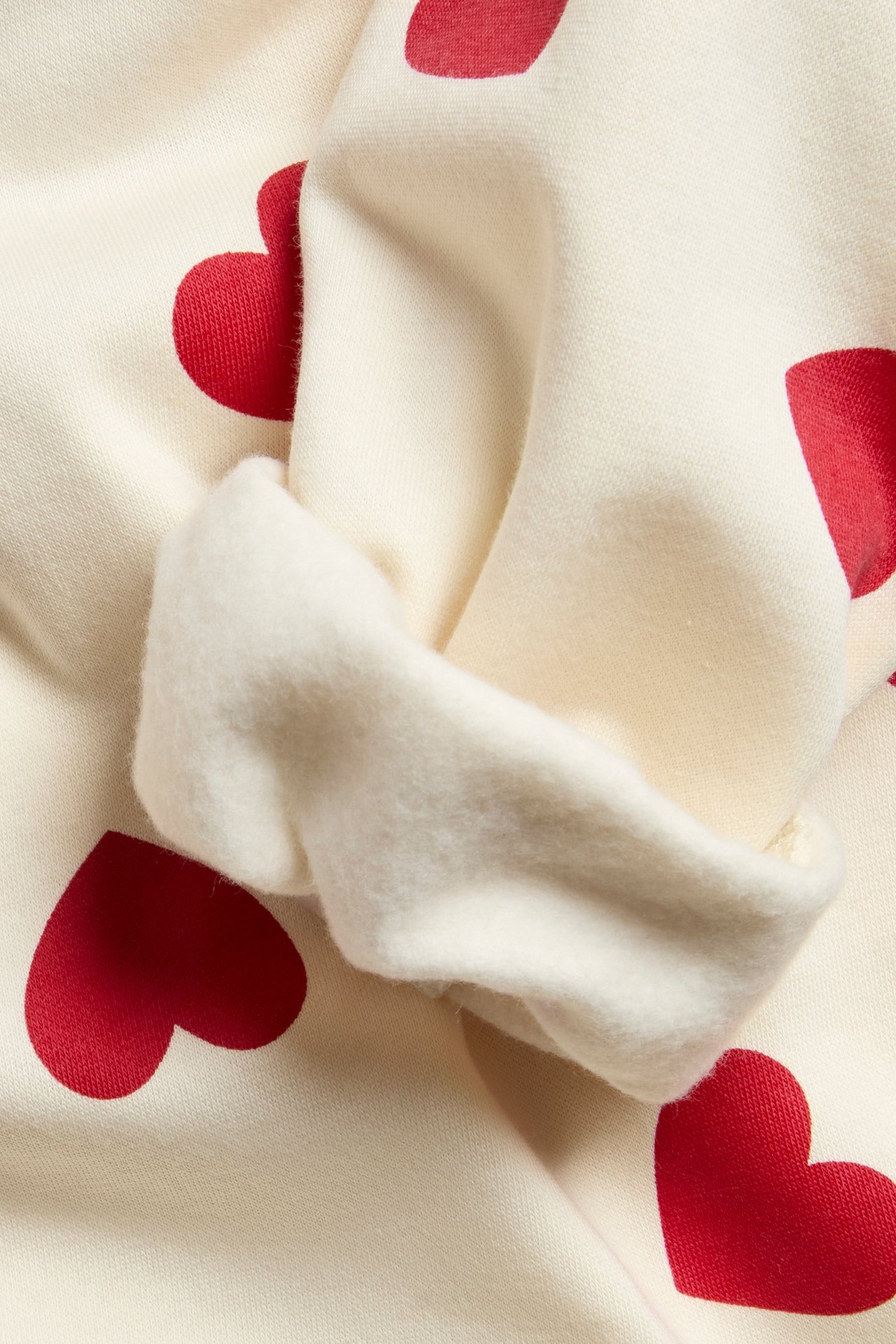 Zbliżenie: Bluza off-white w czerwone serca, pokazująca miękki, szczotkowany materiał wewnątrz podwiniętego rękawa.
