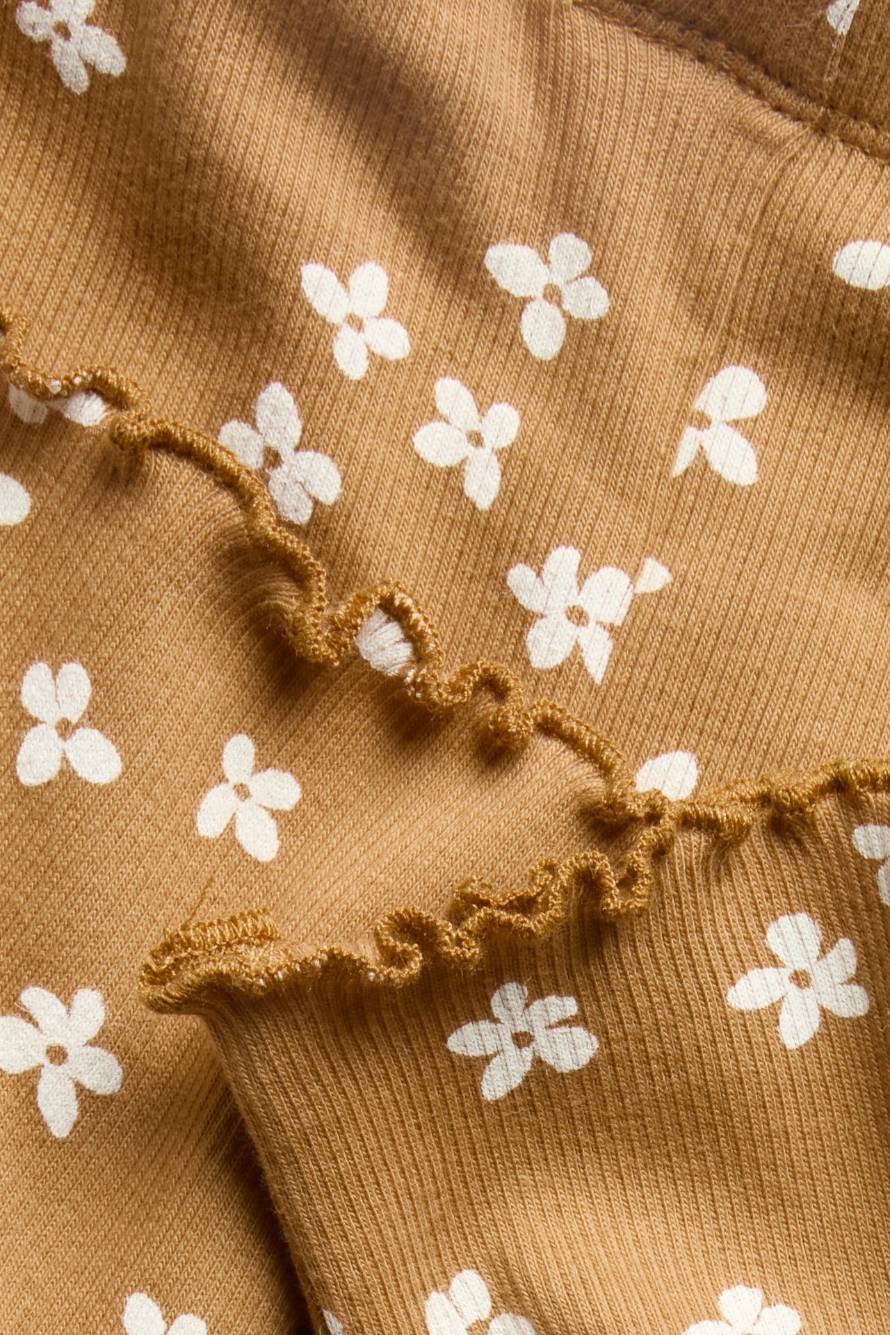 Zbliżenie brązowych, prążkowanych legginsów niemowlęcych z białym kwiatowym wzorem i falbanką.