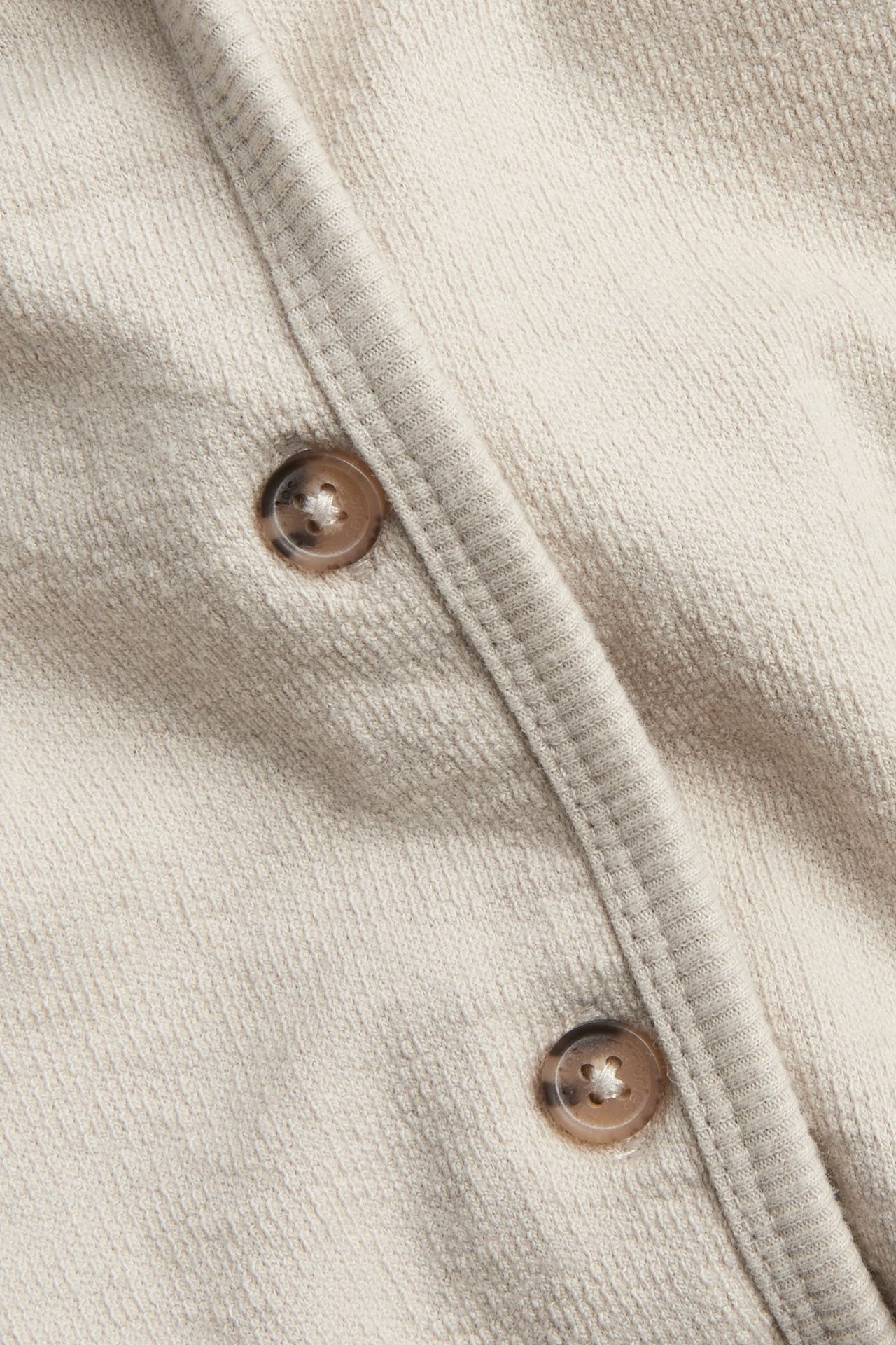Zbliżenie beżowego, jednolitego, bawełnianego swetra niemowlęcego z brązowymi guzikami z przodu.