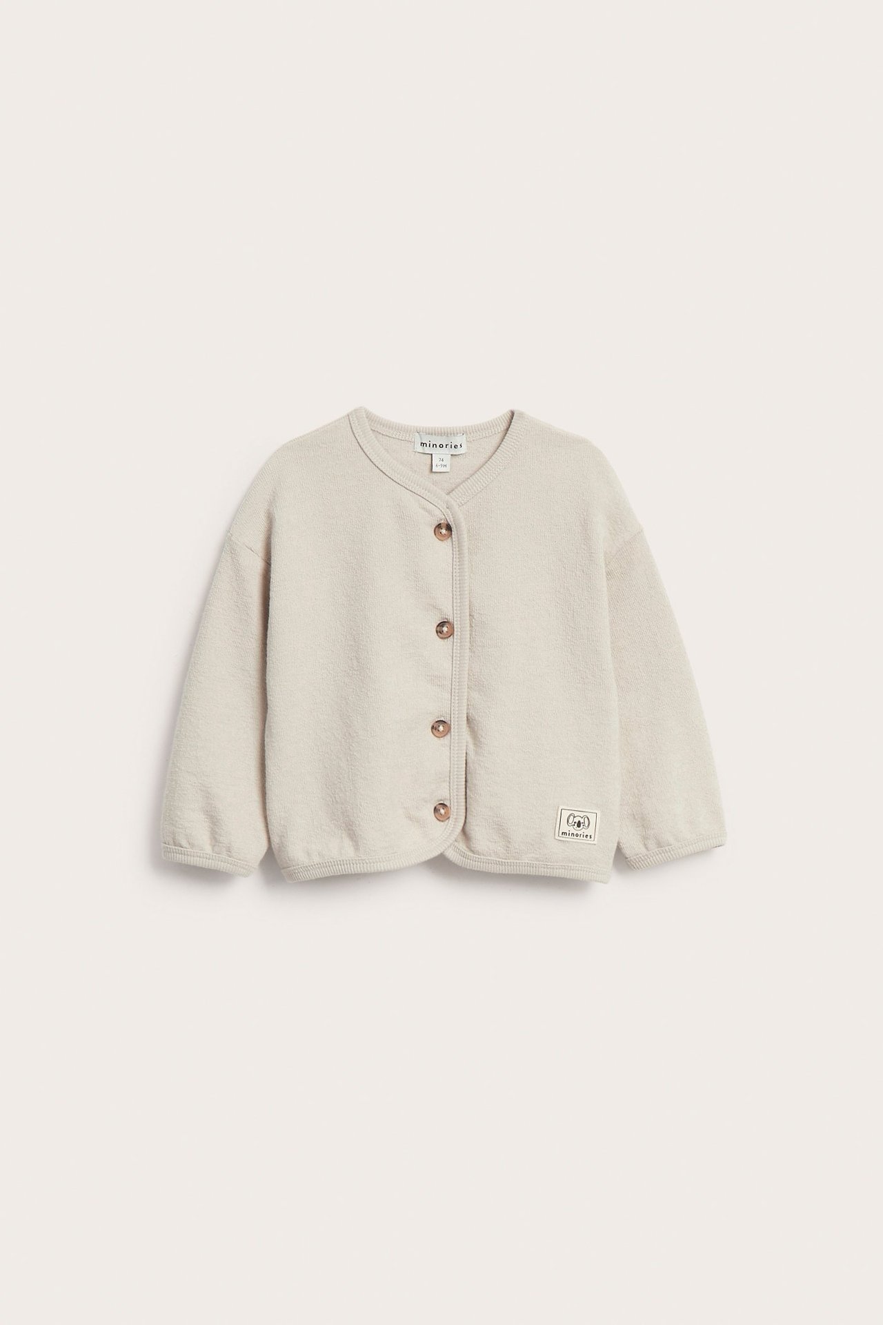 Edestäpäin, yksivärinen beige puuvillaneuletakki vauvalle napeilla edessä.