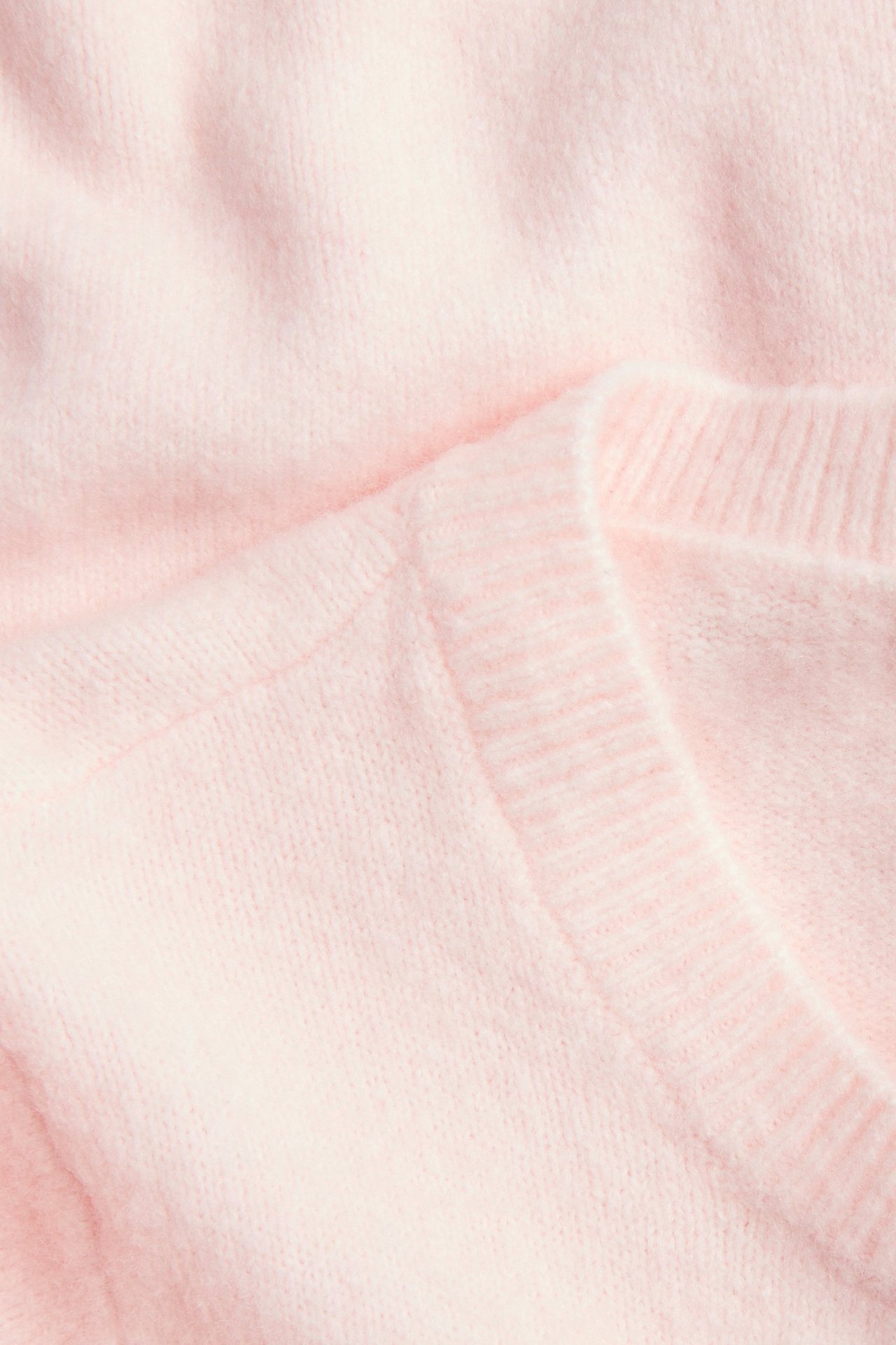 Närbild av en ljusrosa melerad stickad topp med ribbad rund hals.