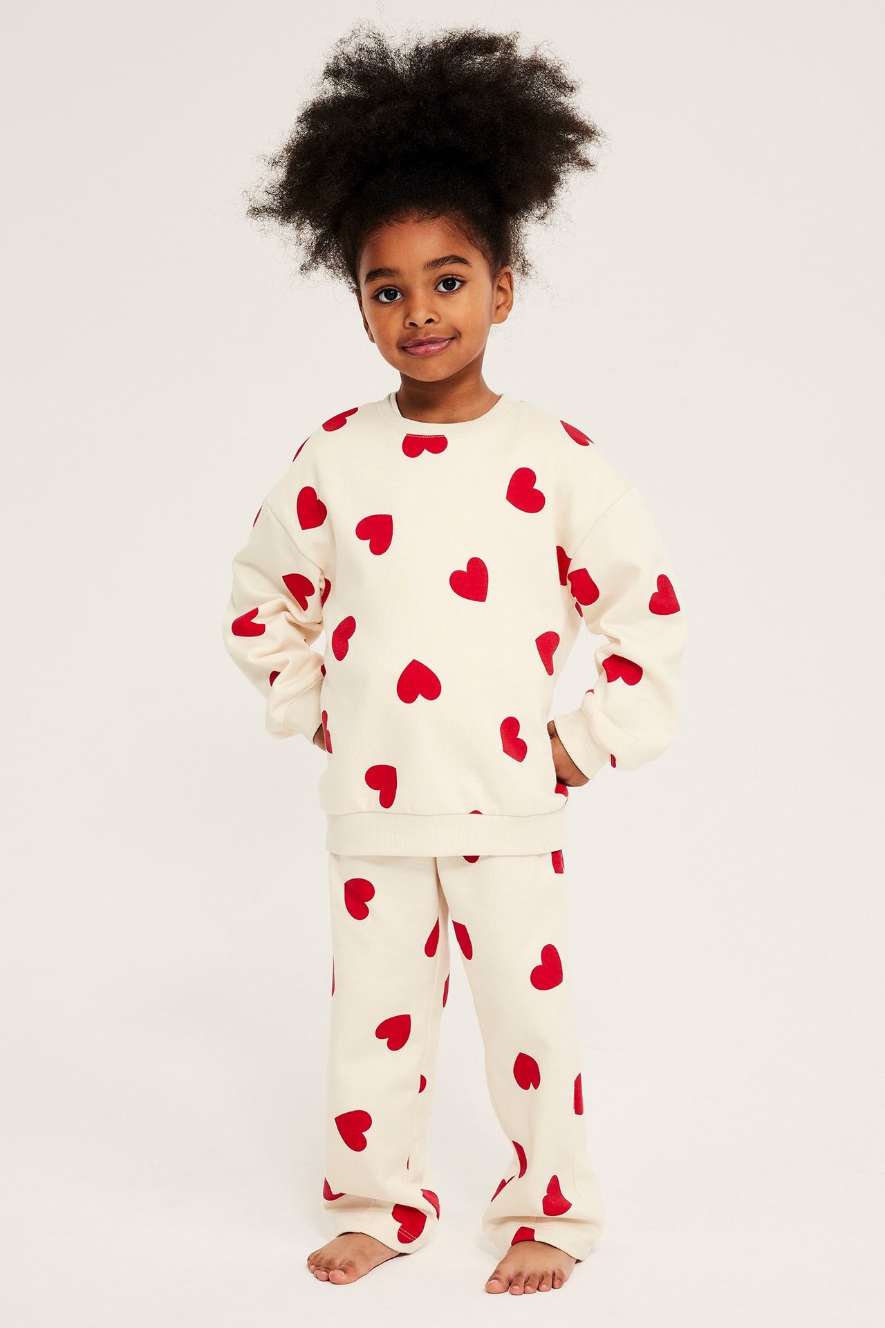 Framifrån: Kid i offwhite mjukisbyxor och matchande sweatshirt, båda med röda hjärtan.