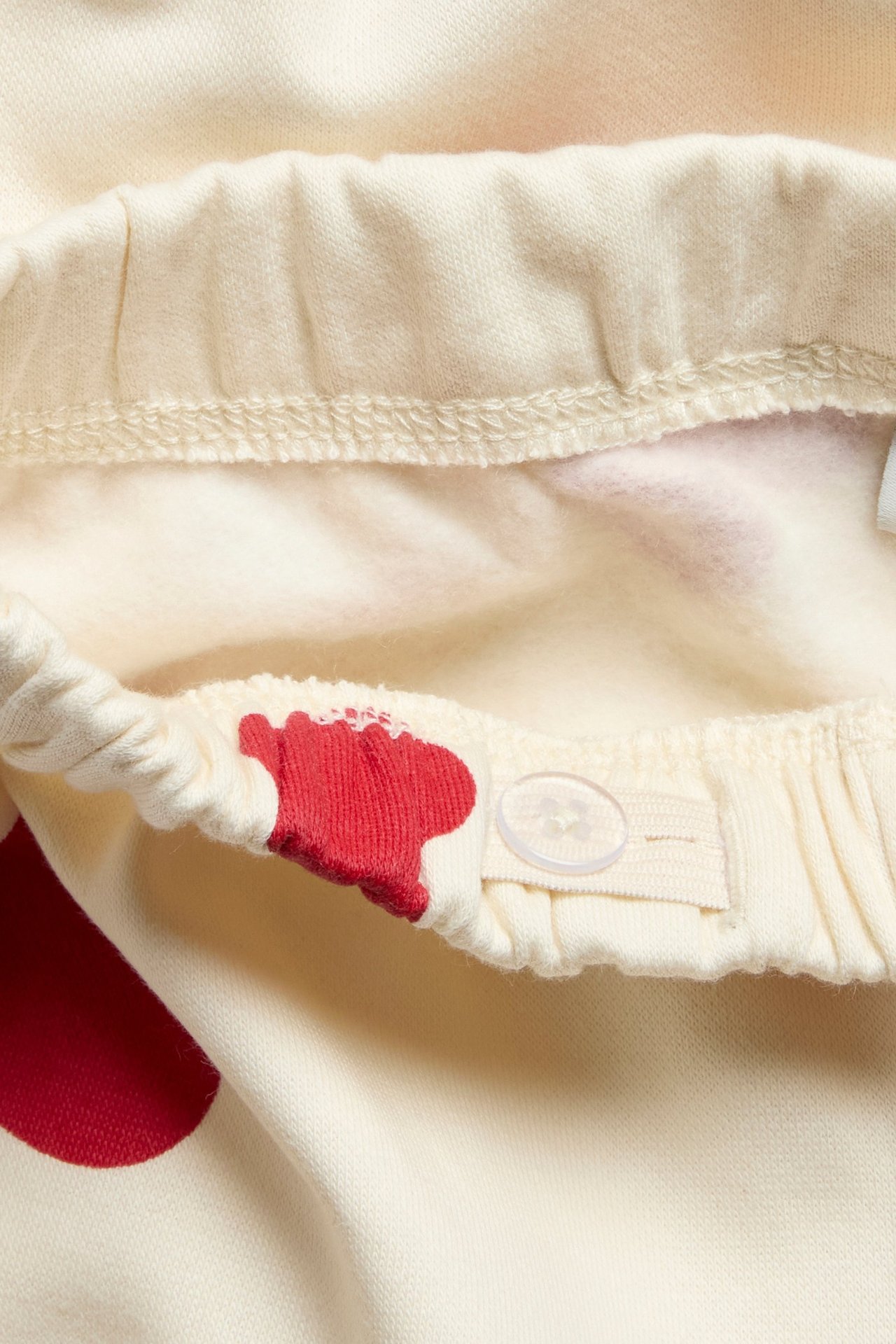 Zbliżenie na off-white dziecięce dresy z czerwonym wzorem serc i regulowaną gumką z guzikiem.