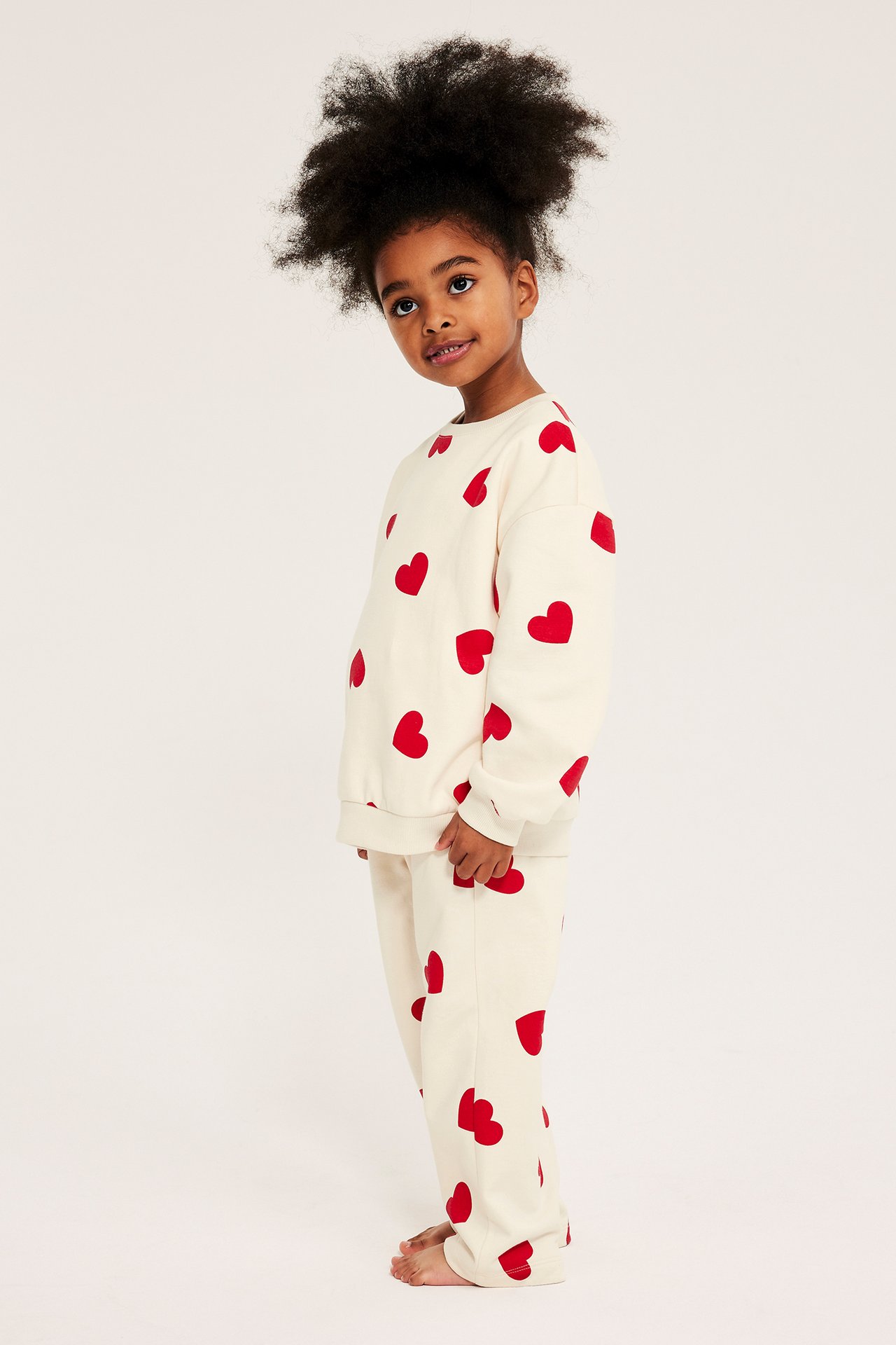 Widok z boku dziecka w miękkim, kremowym zestawie dresowym z czerwonymi sercami.