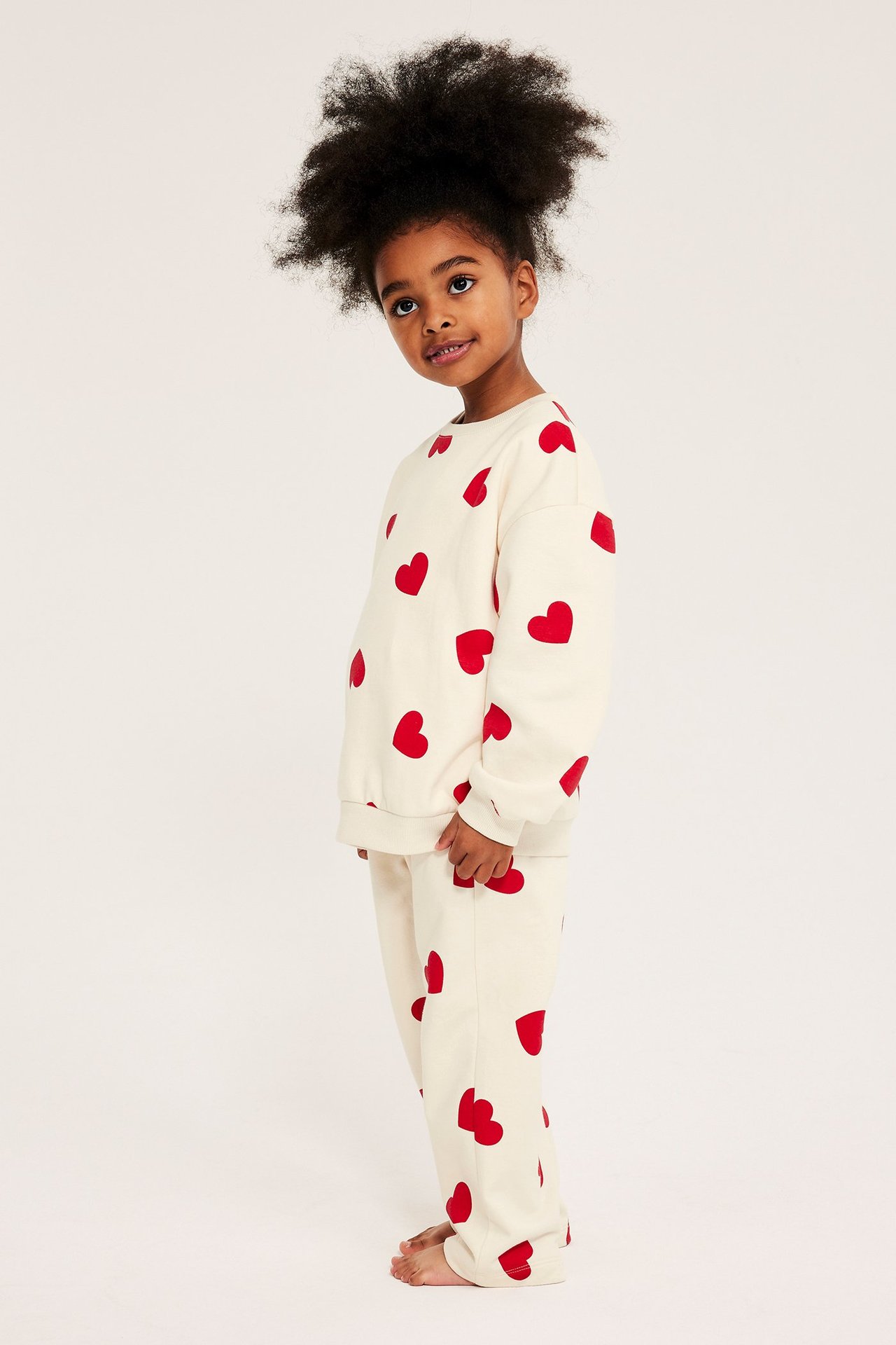 Widok z boku dziecka w miękkim, kremowym zestawie dresowym z czerwonymi sercami.