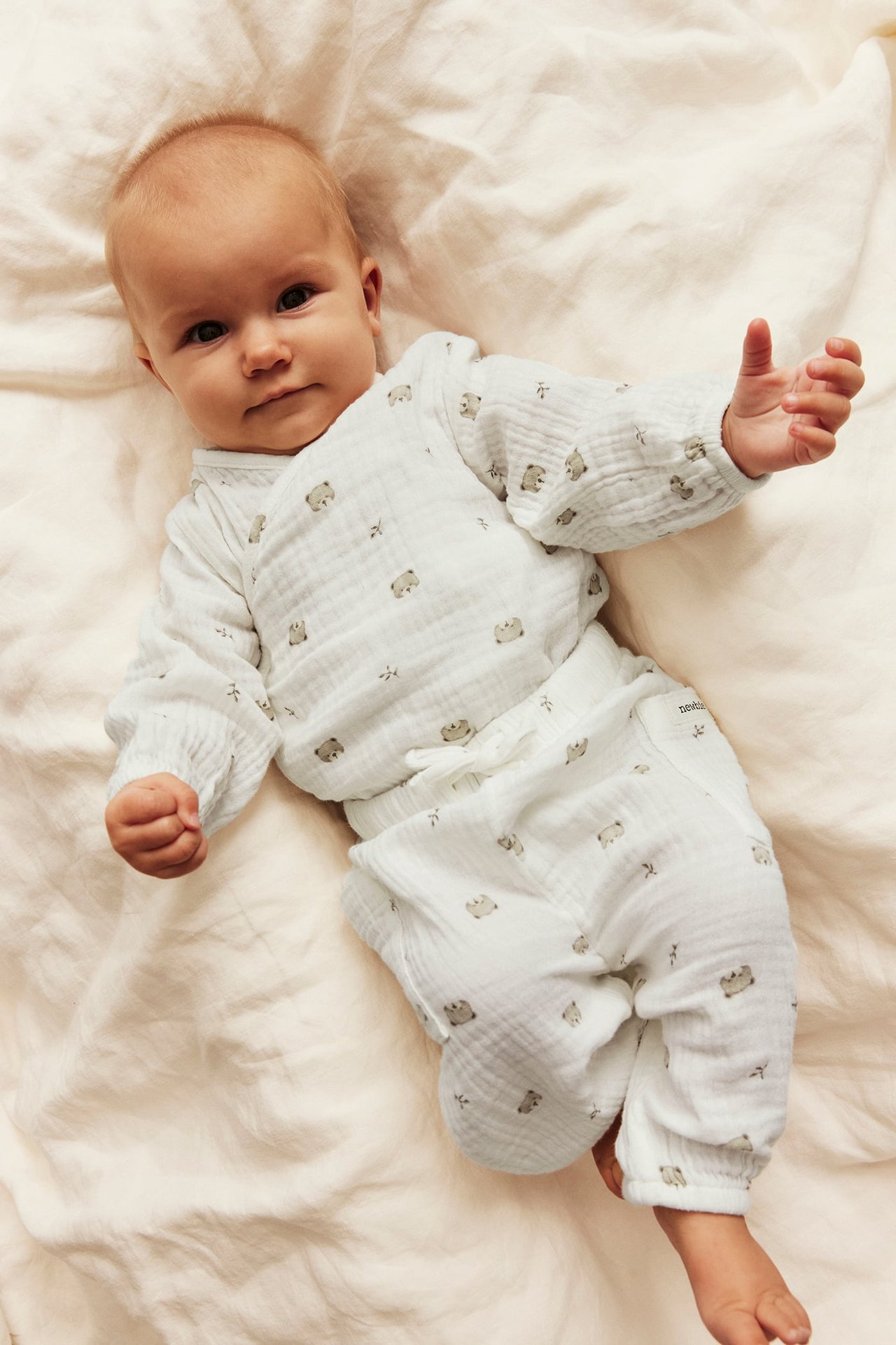 Uppifrånvy av baby i vit muslintröja och byxor med björnmönster.