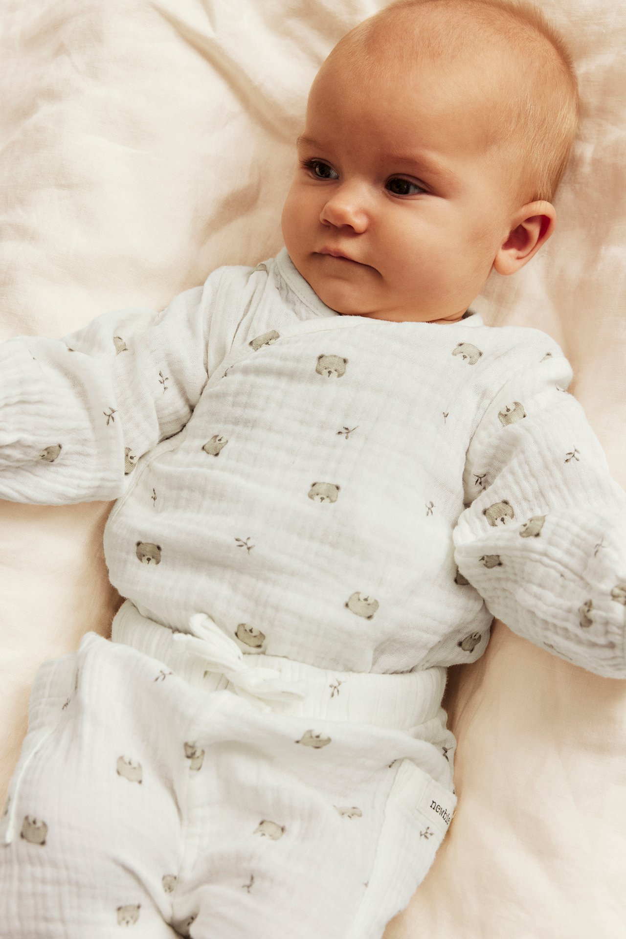 Ovanifrån, baby i vit muslin omlott-topp med björntryck och matchande byxor.