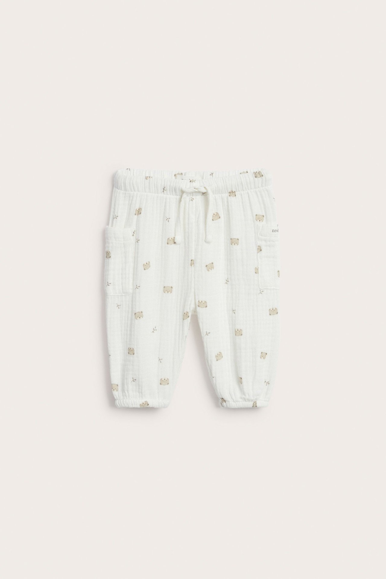 Frontbilde: Offwhite babybukse i bomullsmuslin med bjørneprint, elastisk snøring i livet og to påsydde lommer.