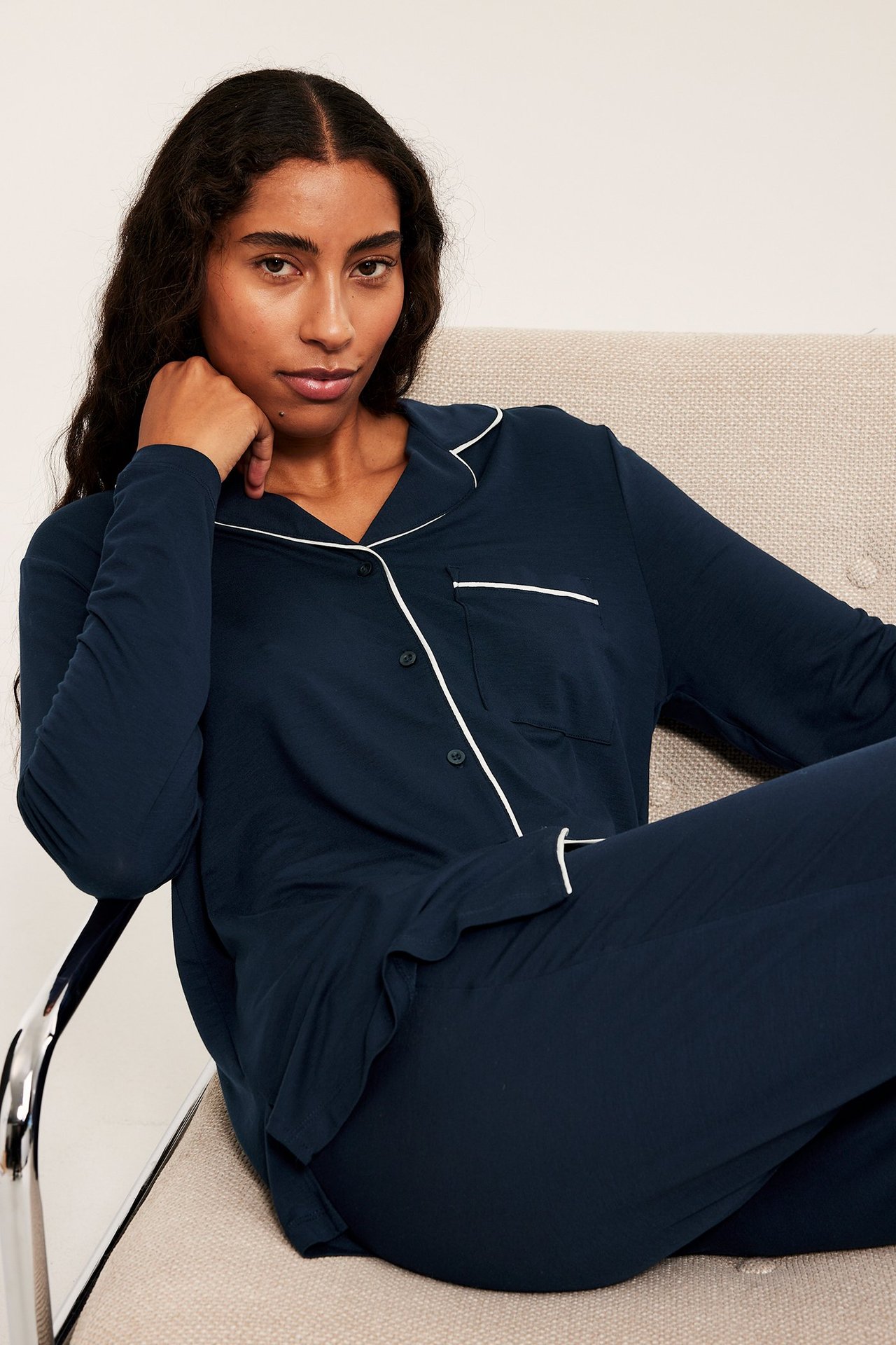 Nainen tummansininen lyocell-pyjamas, istuu tuolilla, etukulma.