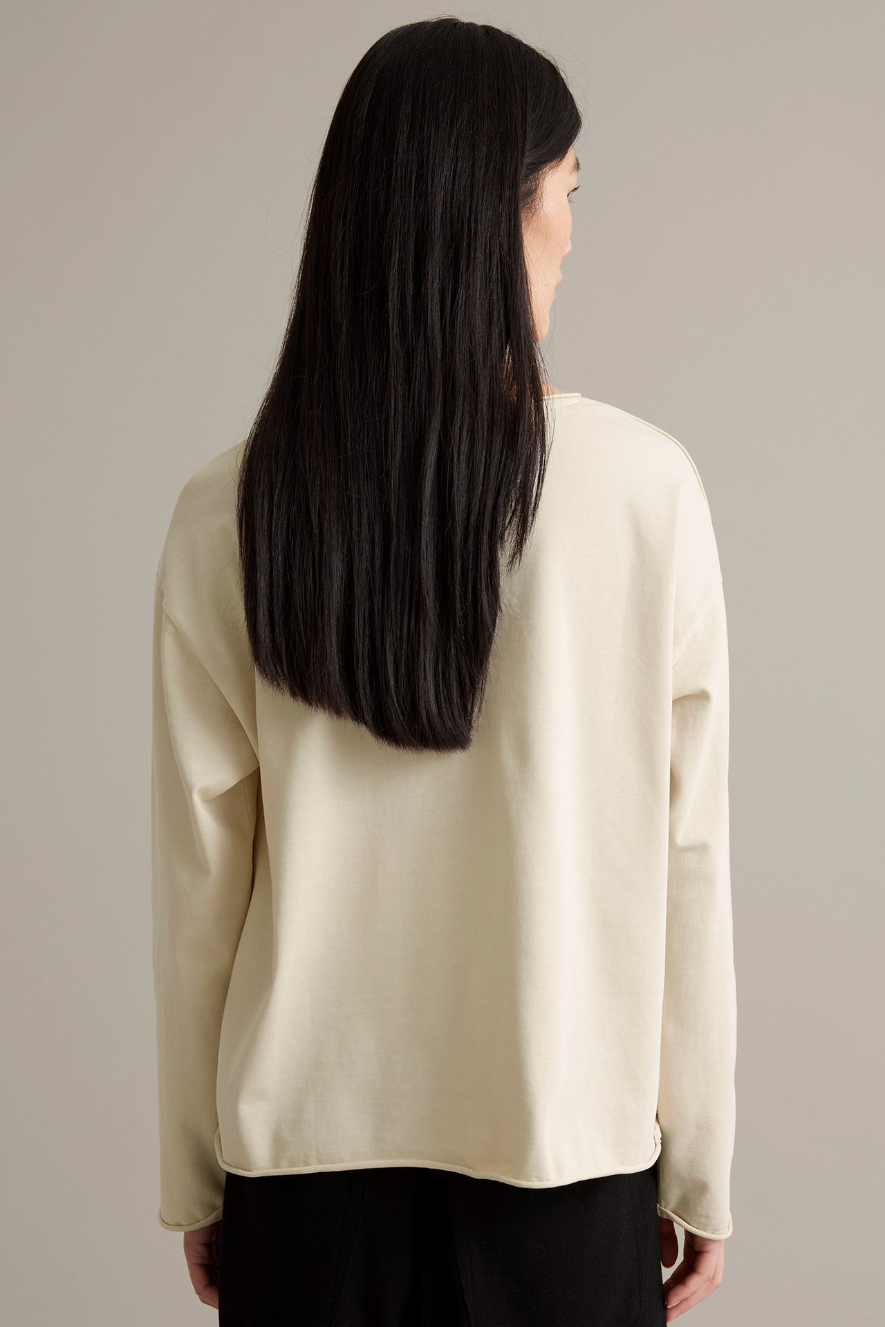 Kvinnlig modell i beige långärmad tröja av kraftig trikå, rullande kanter, tvättad look.